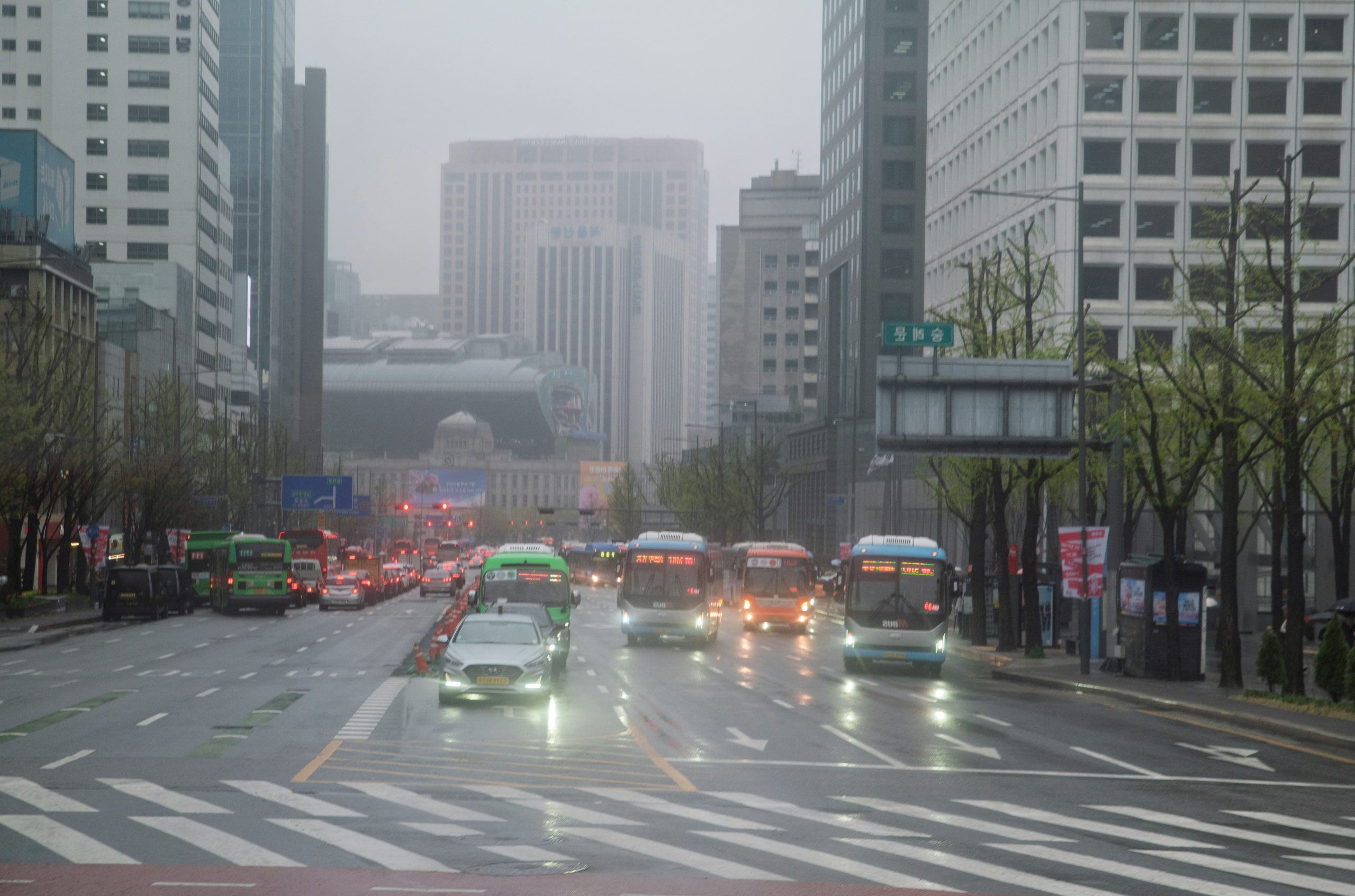 Buses and cars driving on a wet city street.