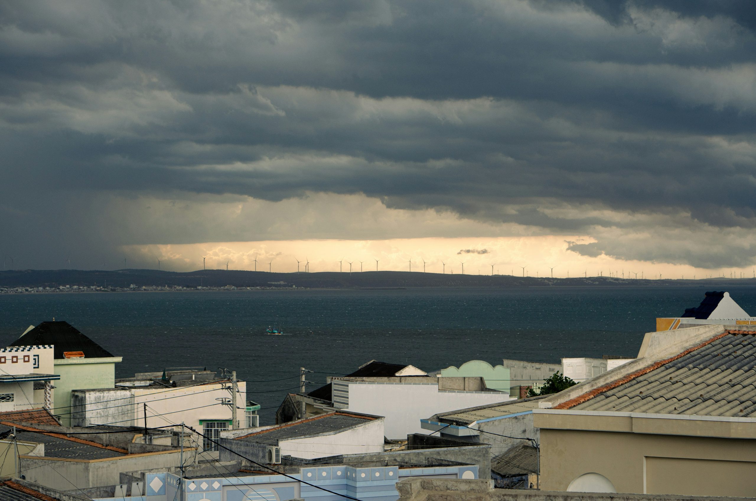 Dark storm clouds gather over the sea and rooftops.