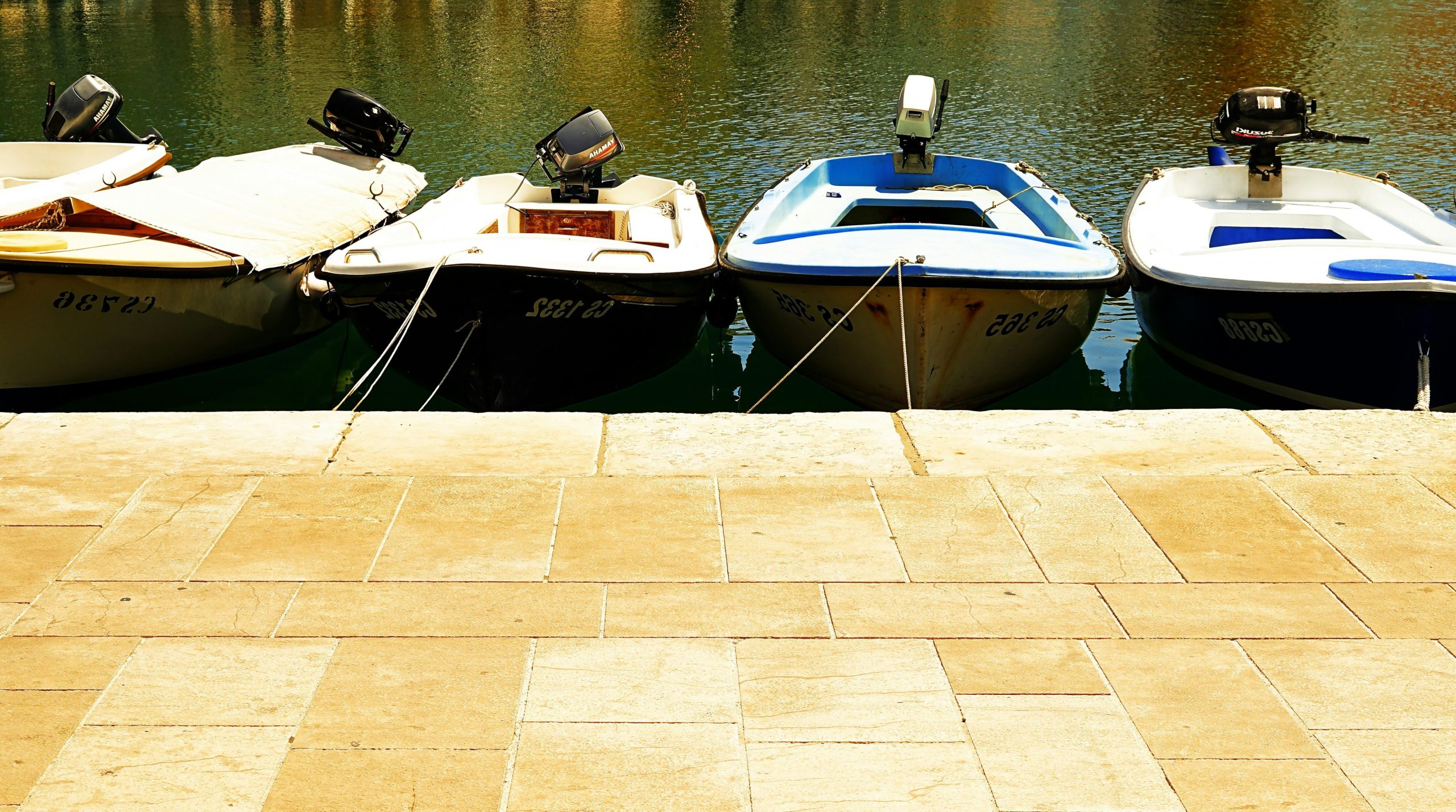 Four small boats docked by a stone walkway.