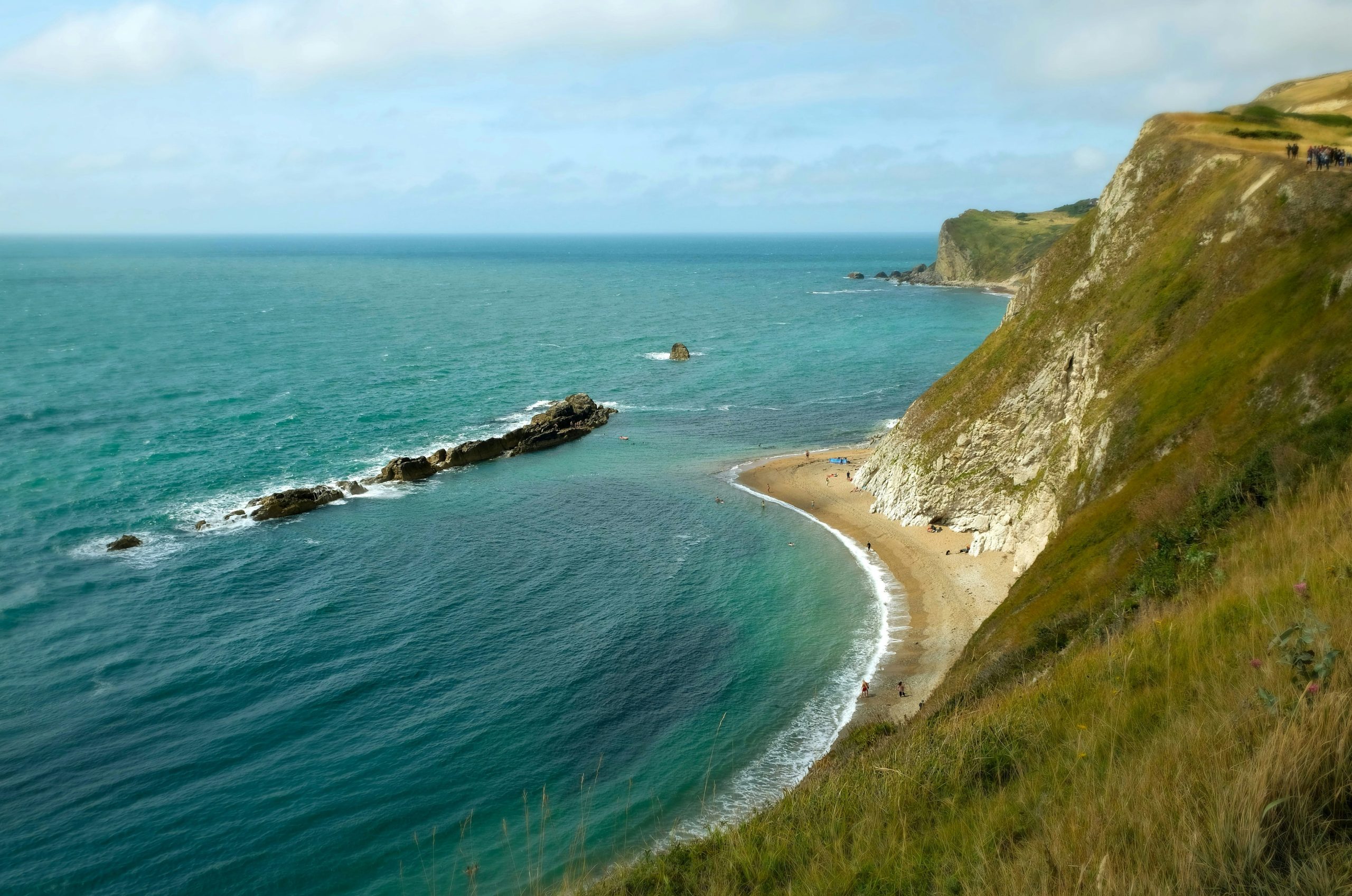 Green cliffs meet the turquoise ocean with a small beach.