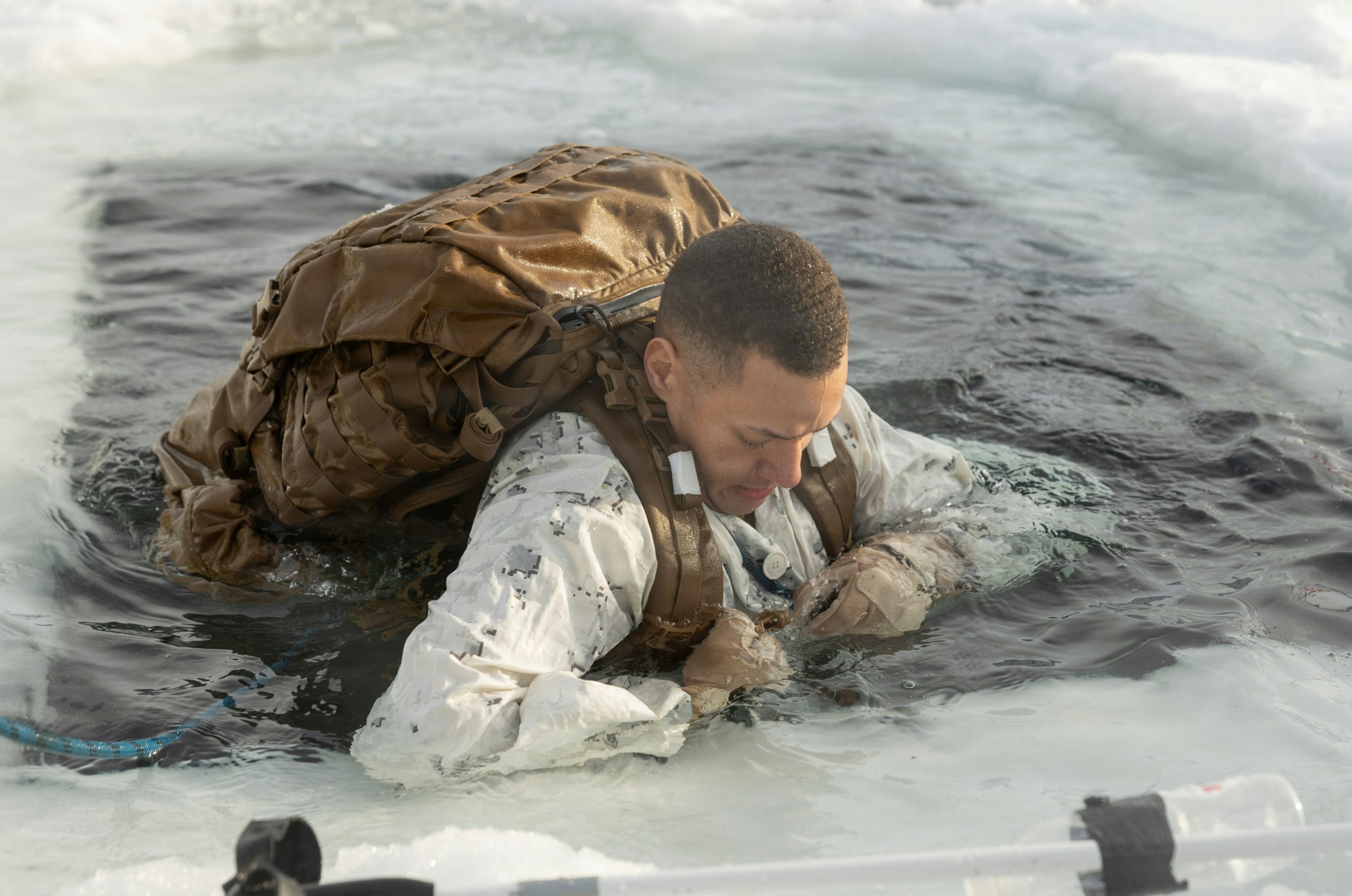 Man in camouflage climbing out of icy water