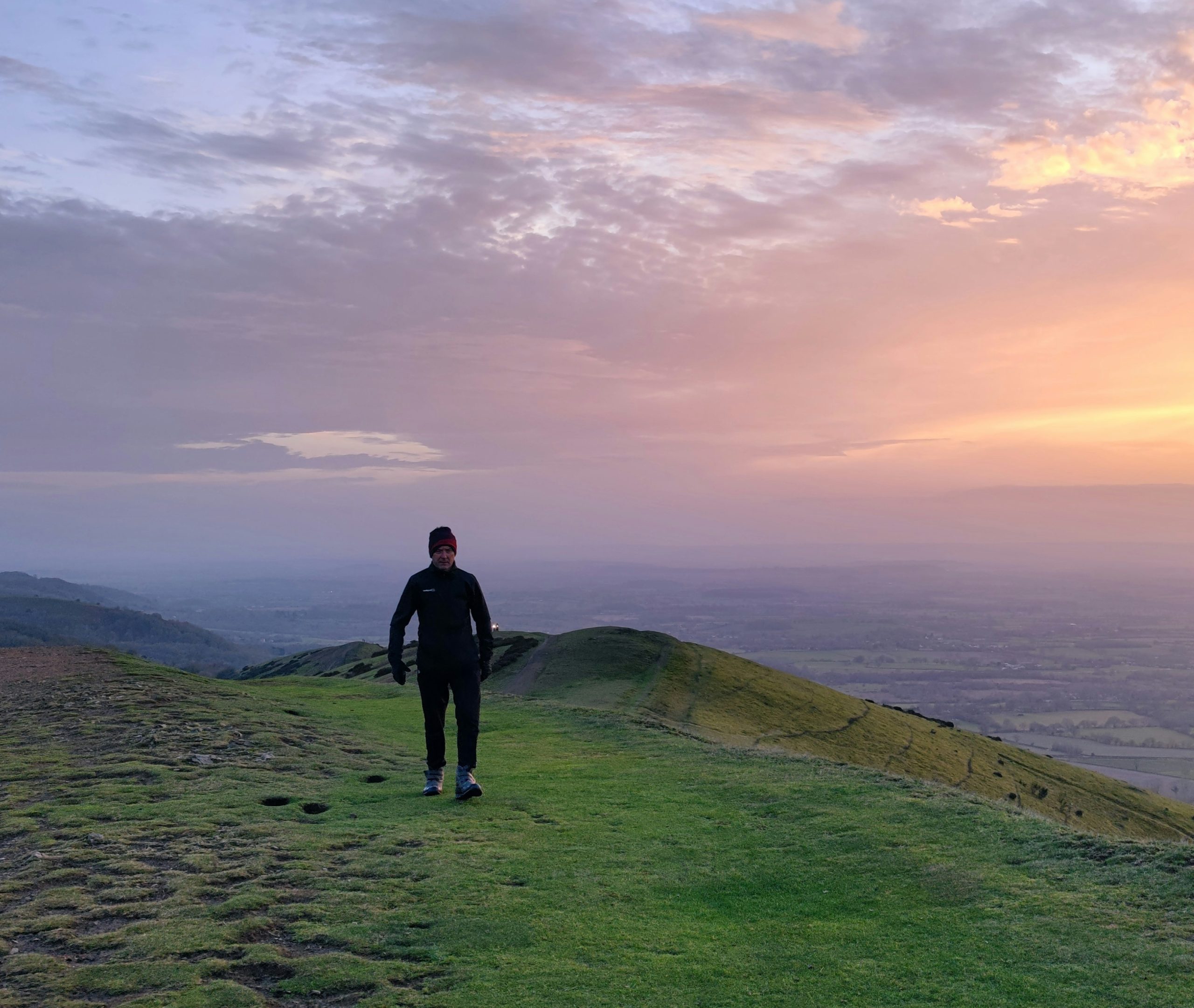 Man walking on a grassy hill at sunset