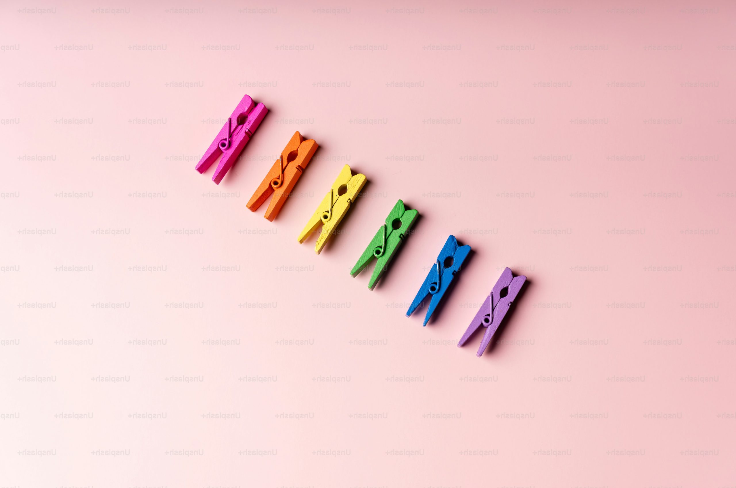 Six colorful clothespins arranged diagonally on a pink background