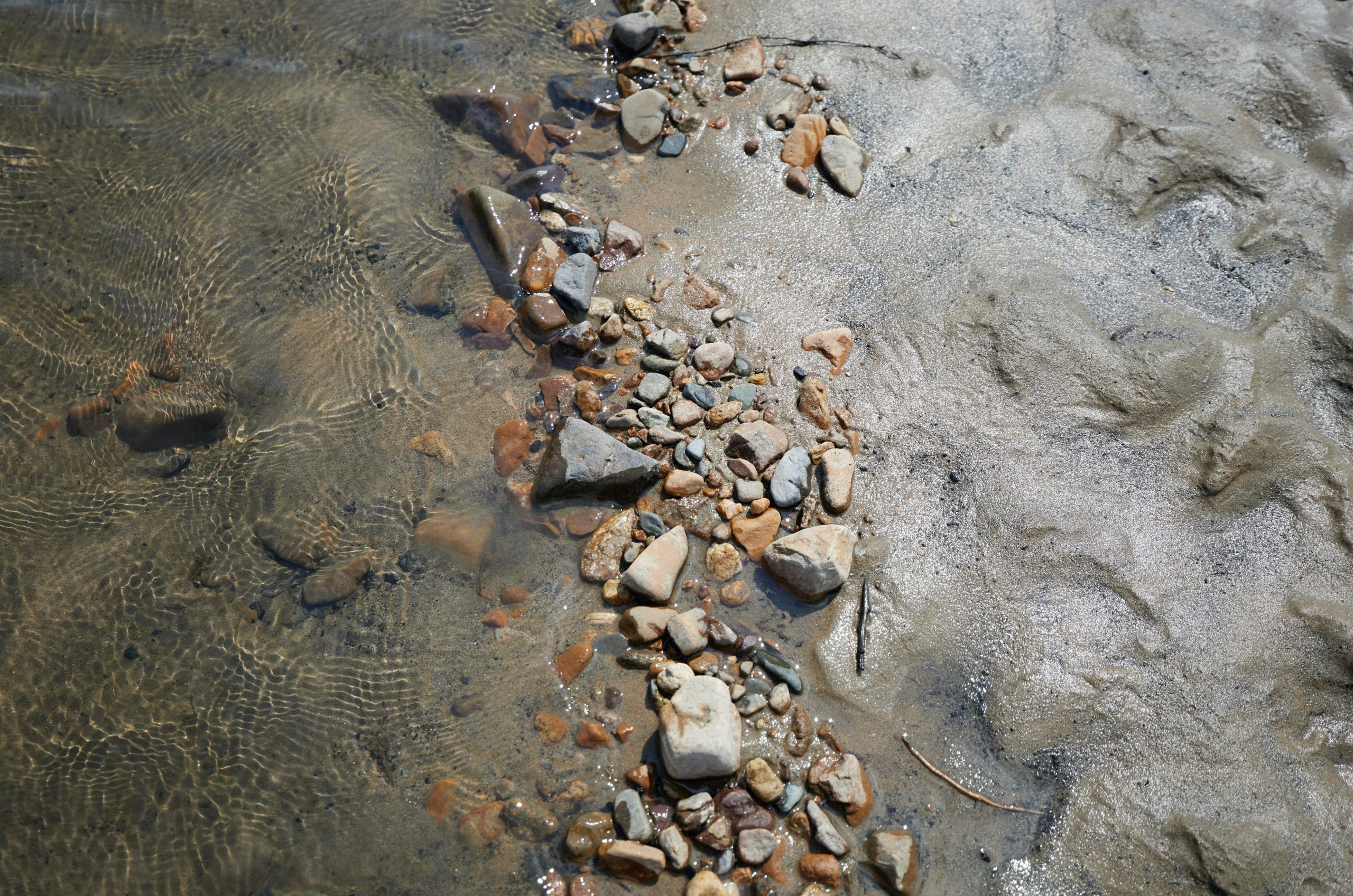 Small rocks and sand on a beach with shallow water.