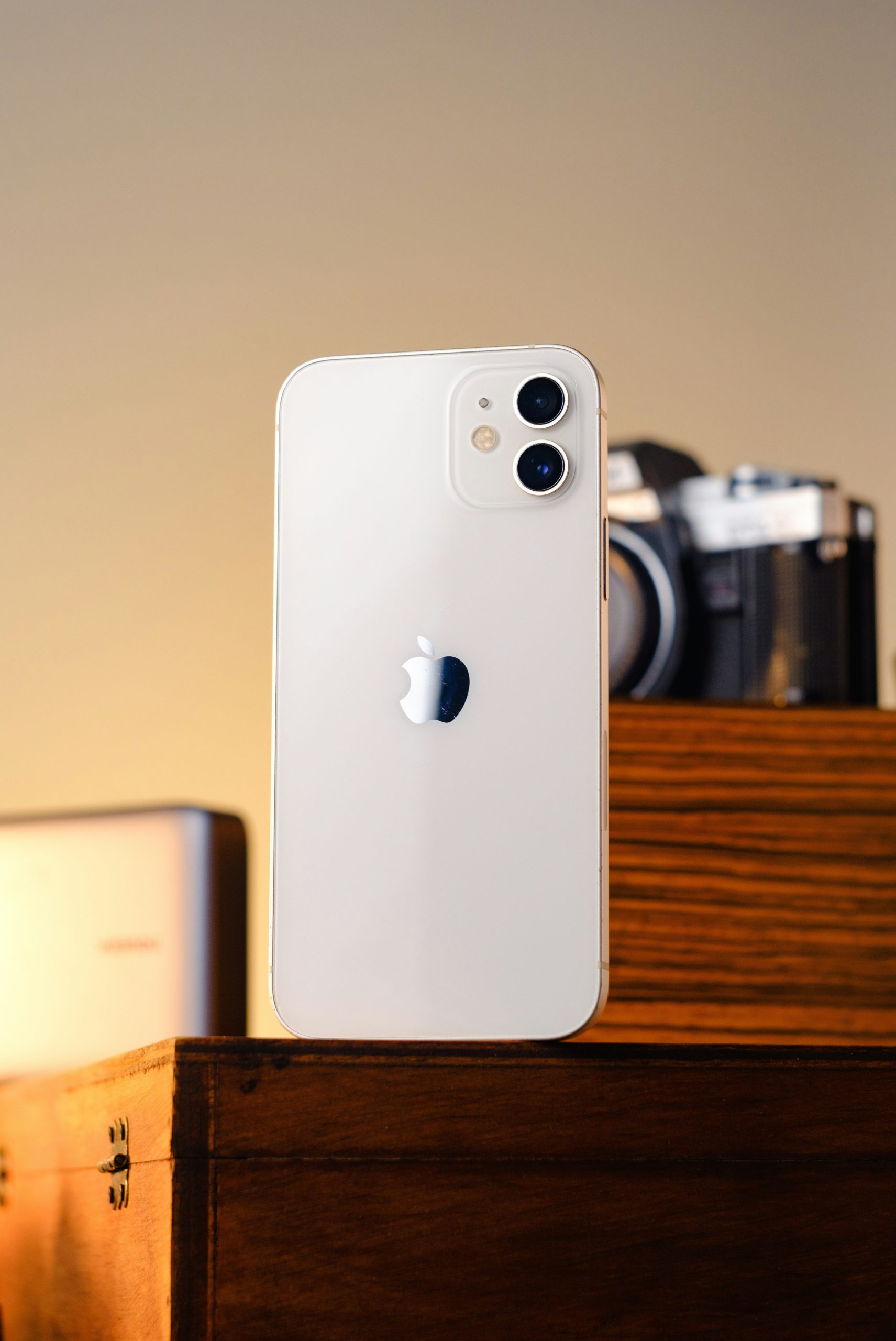 White iPhone 12 on a wooden shelf with camera.
