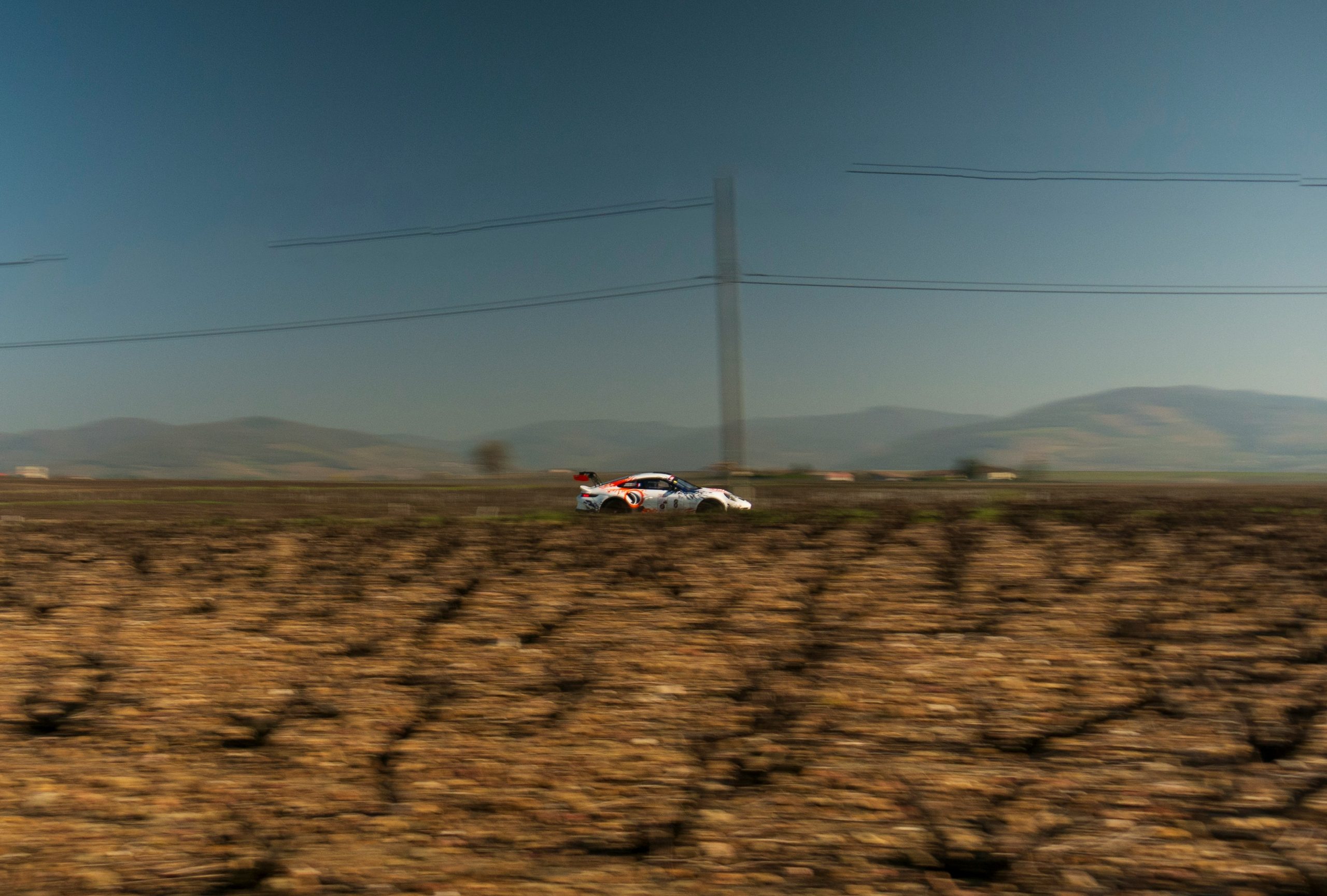 White race car driving through a dry field