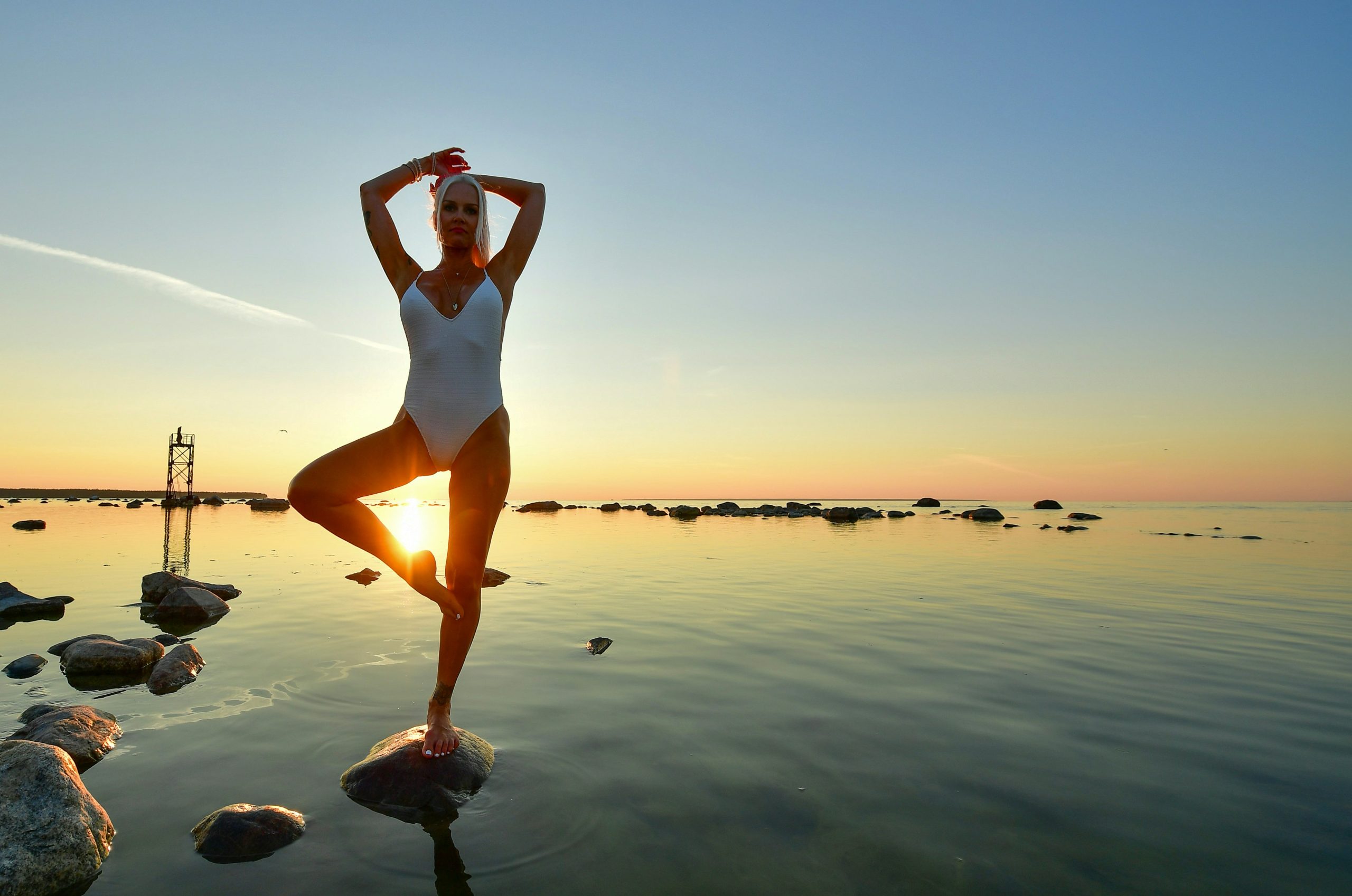 Woman in swimsuit doing yoga by the ocean at sunset
