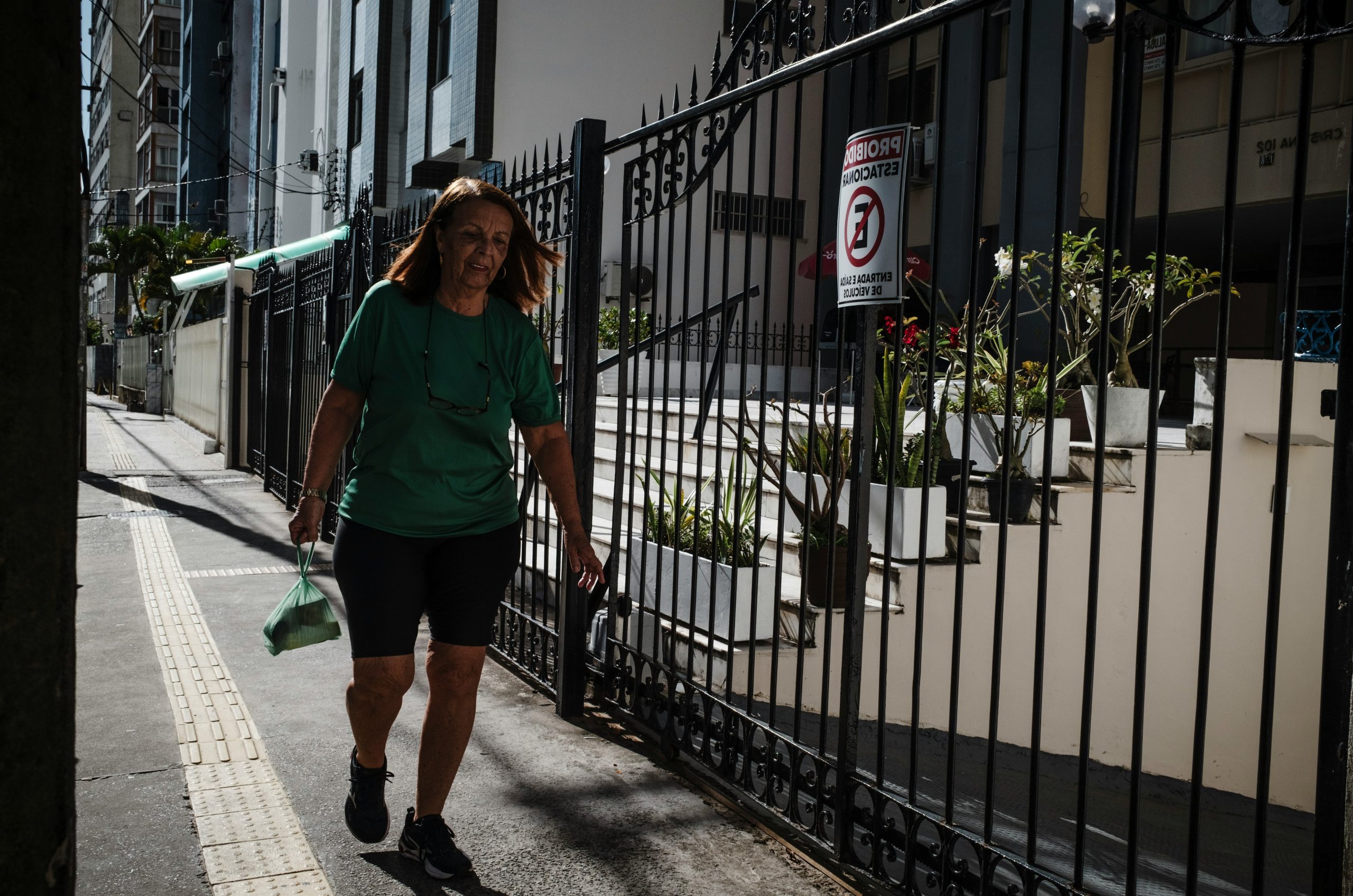 Woman walking on a sidewalk next to a fence.