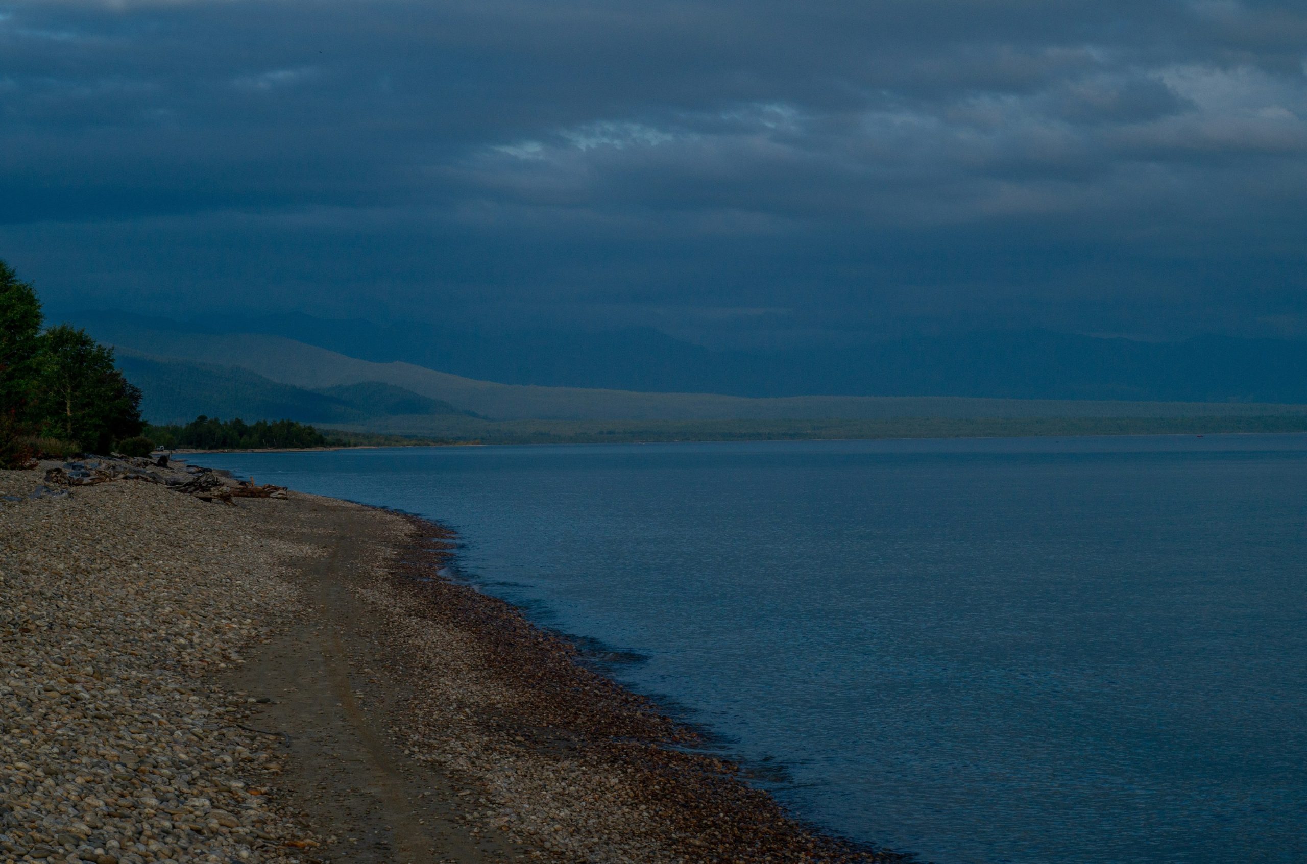 A calm lake shore under a cloudy evening sky.