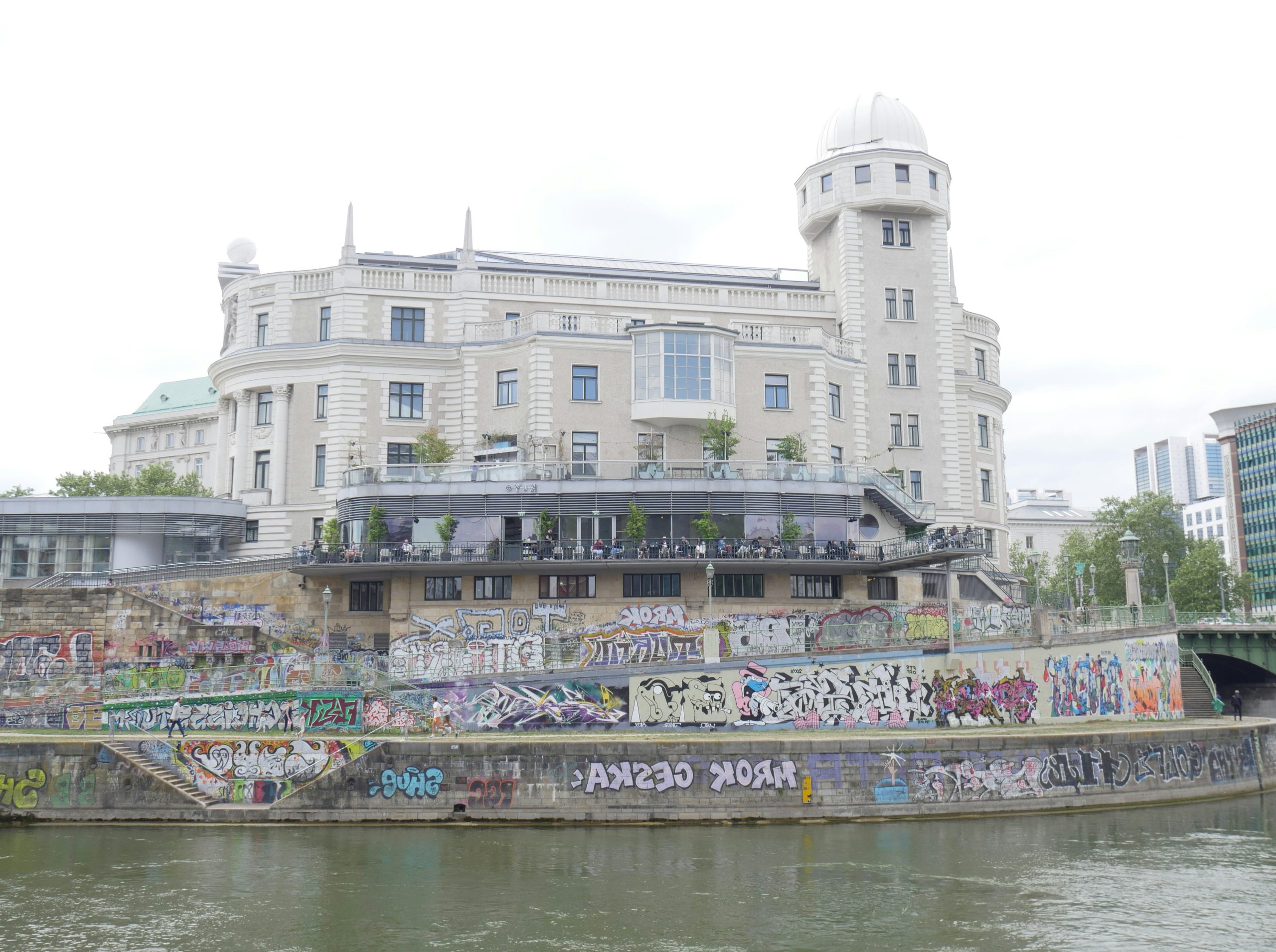 A large building with a dome overlooking a graffiti-covered riverbank.