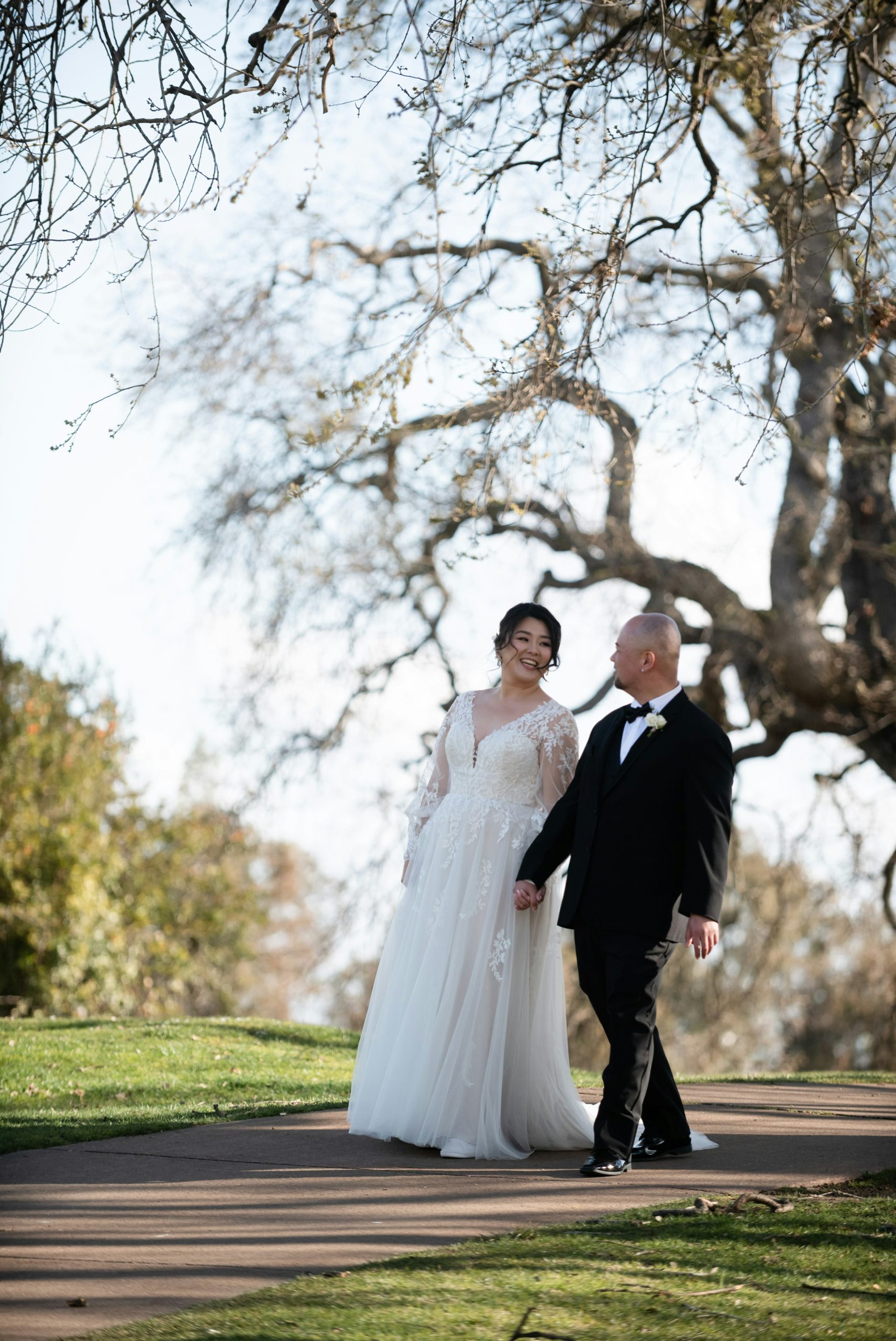 A smiling bride and groom walk hand-in-hand outdoors.