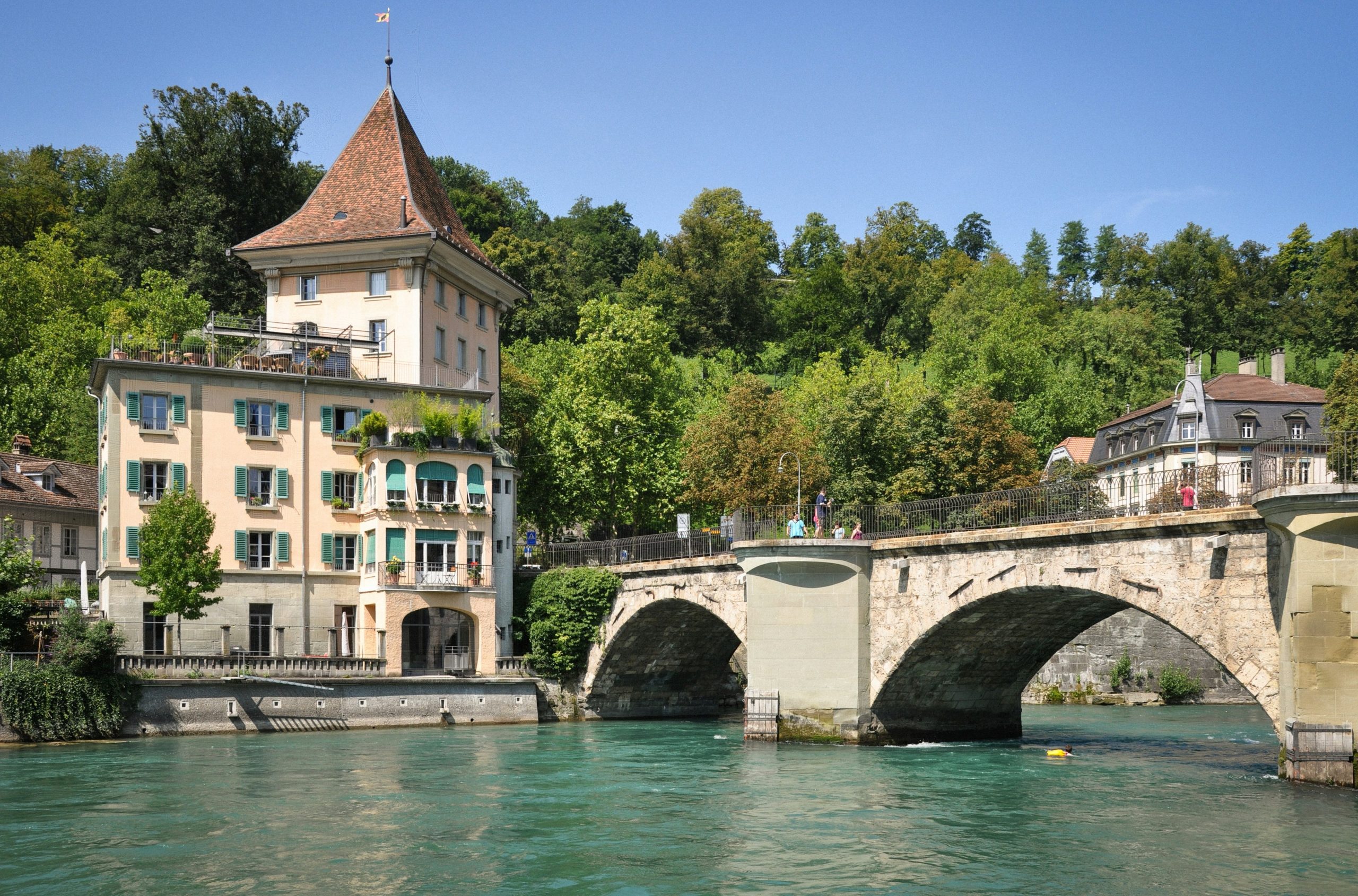 A stone bridge over a turquoise river with historic buildings.