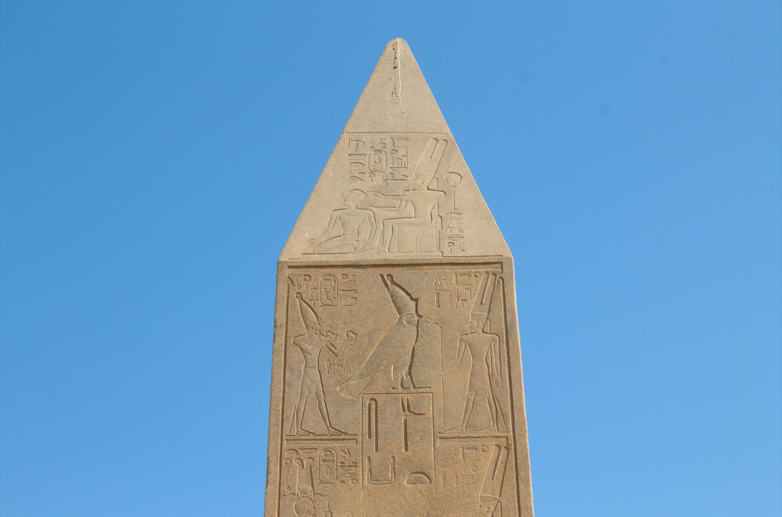 Ancient egyptian obelisk with hieroglyphs against a clear blue sky.
