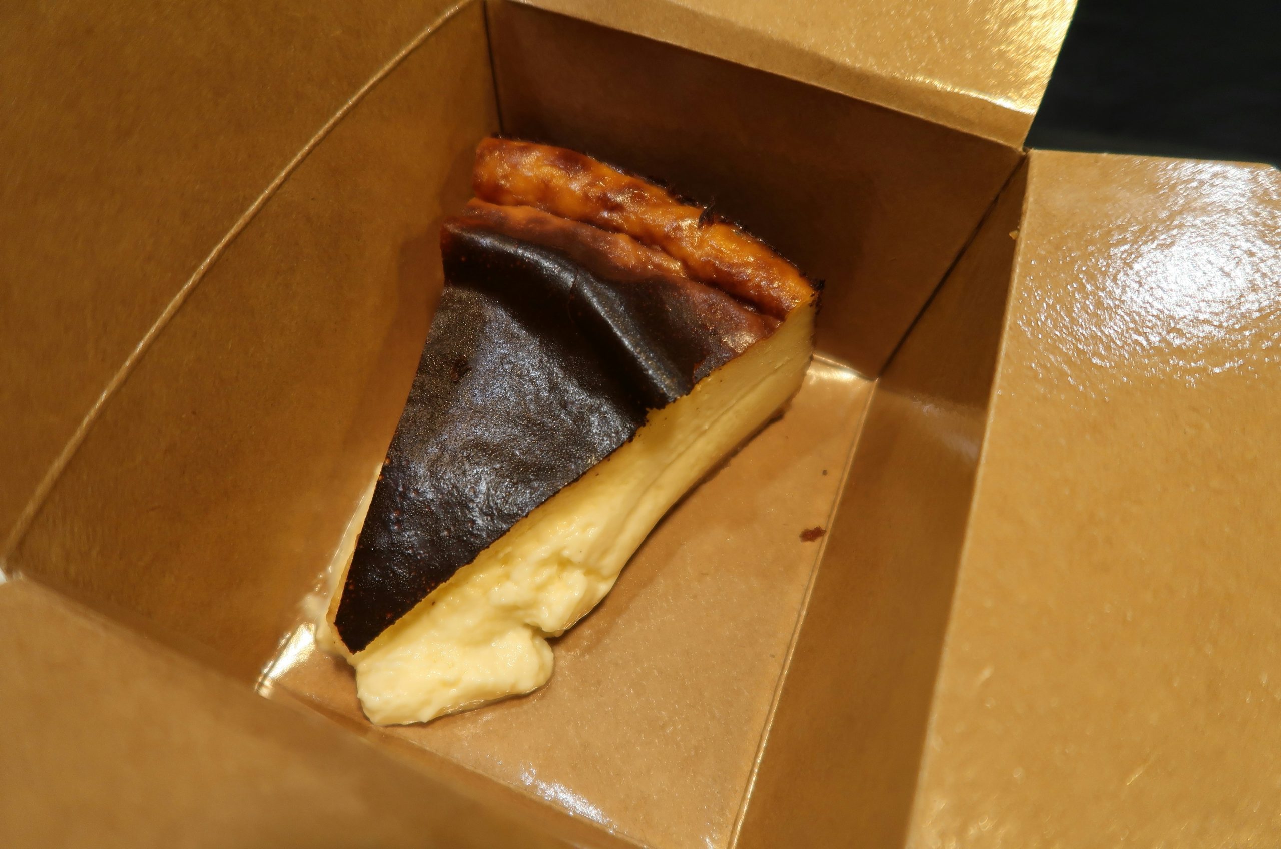 Burnt basque cheesecake slice in a brown cardboard box.