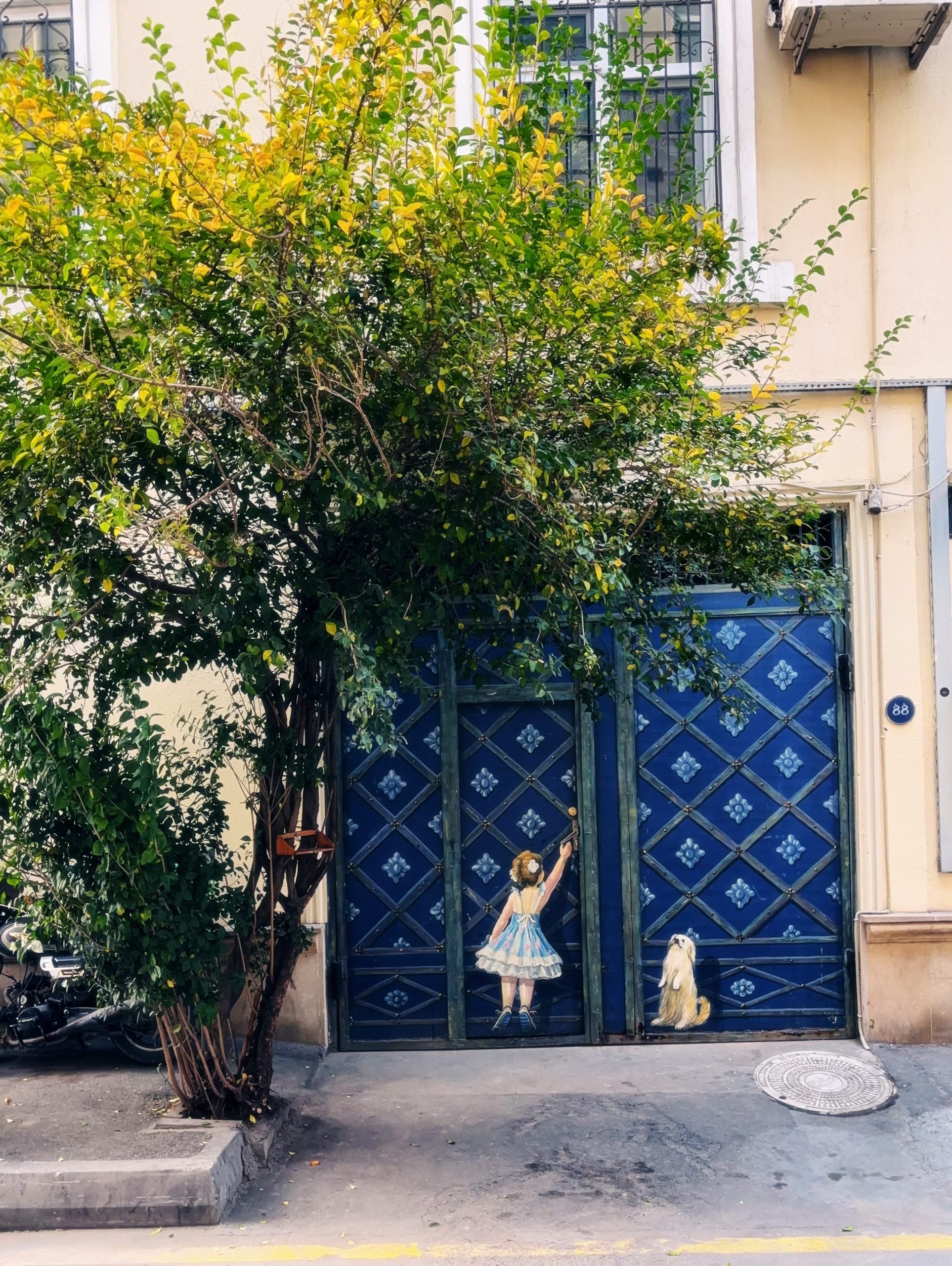 Girl and dog mural on blue gate with a tree.