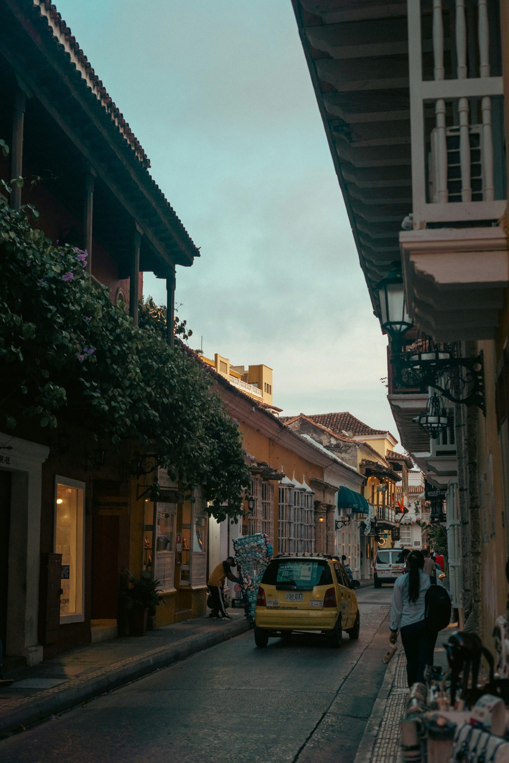 Historic street with balconies, a yellow car, and a pedestrian.