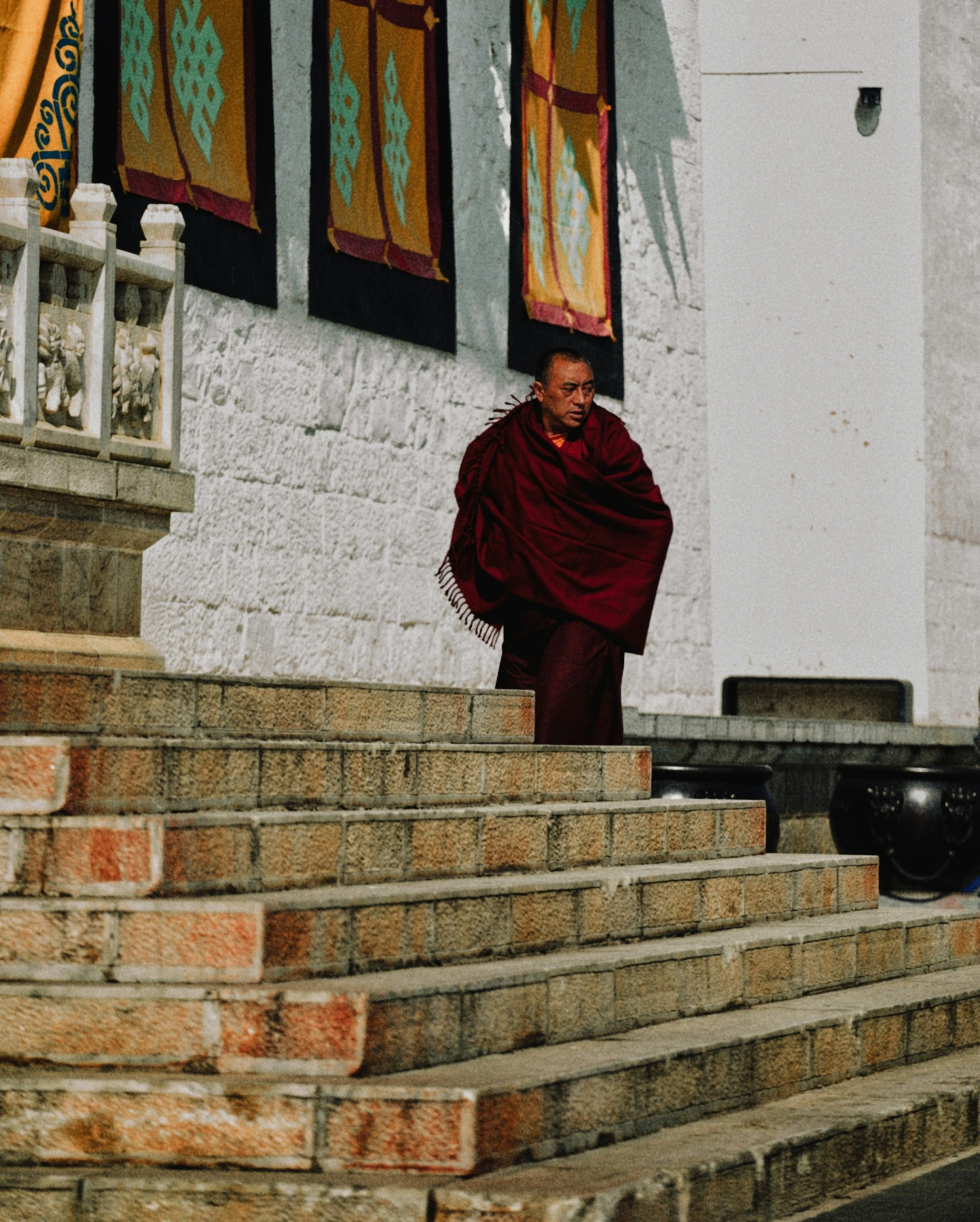 Monk in maroon robe walking down stone steps.
