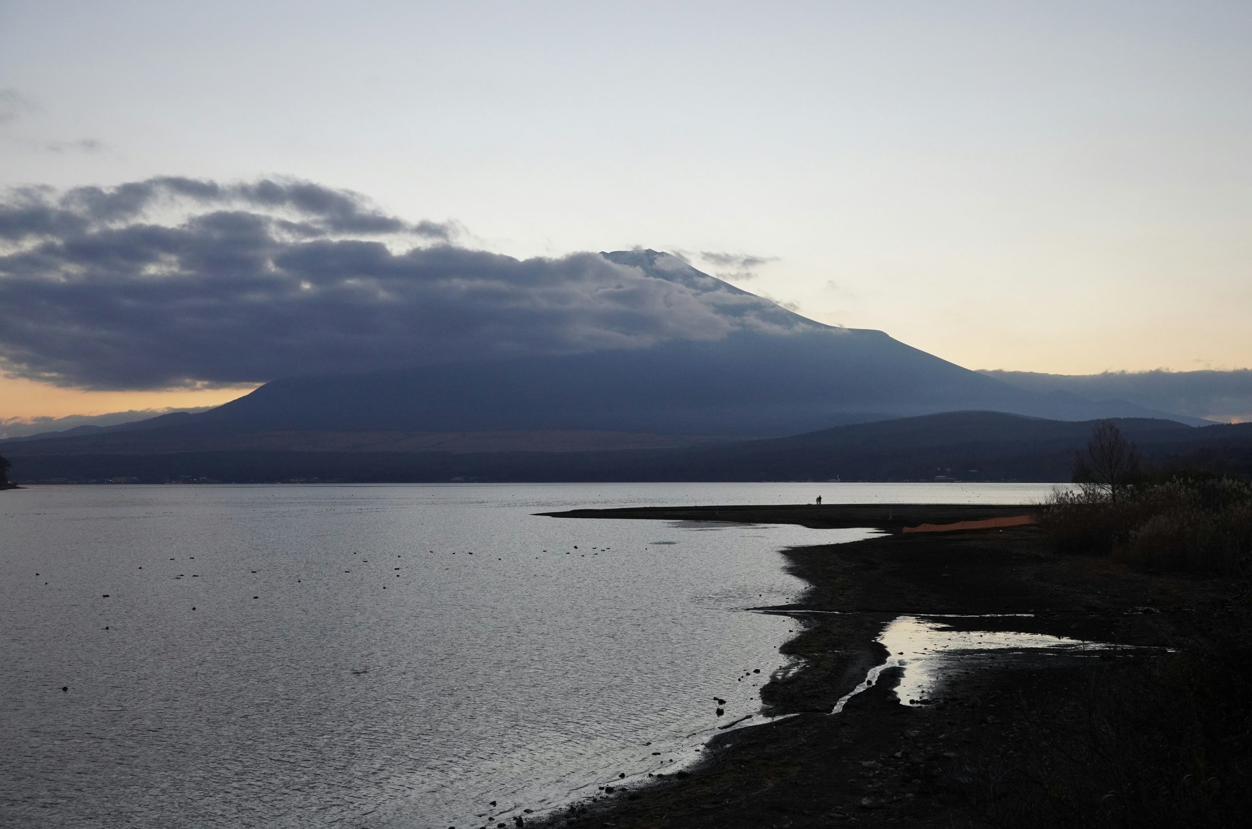 Mountain peak shrouded in clouds over calm lake.