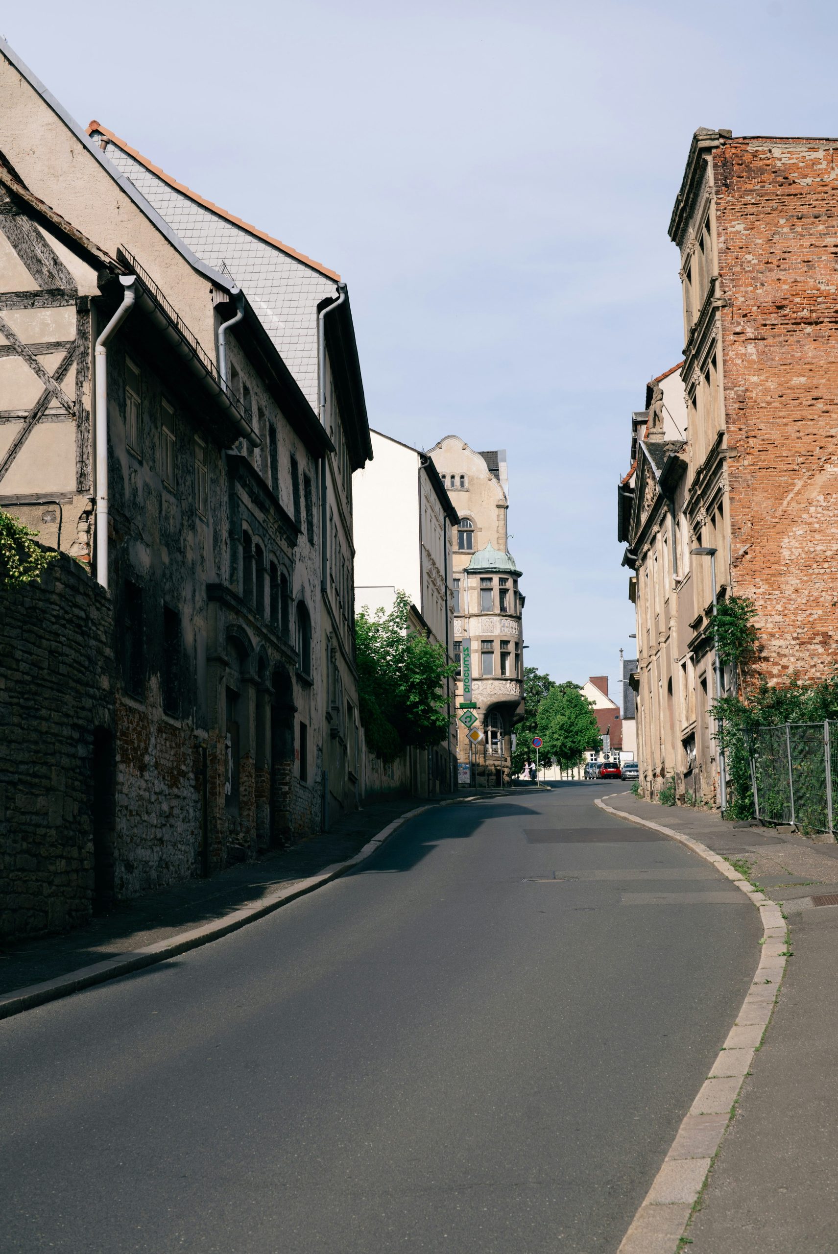 Old buildings line a curving street under a clear sky.