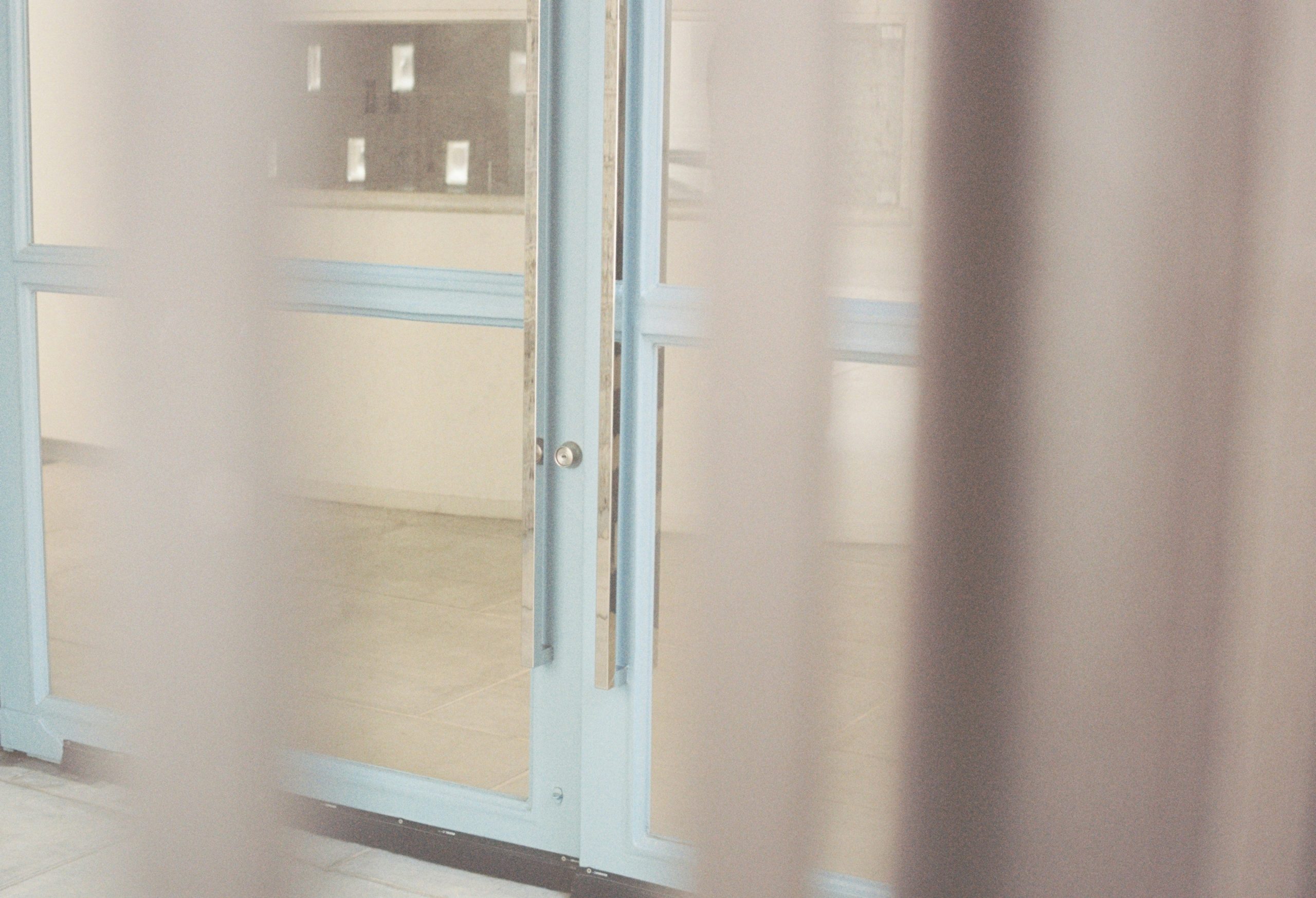 Pale curtains frame a light blue door with glass panels.