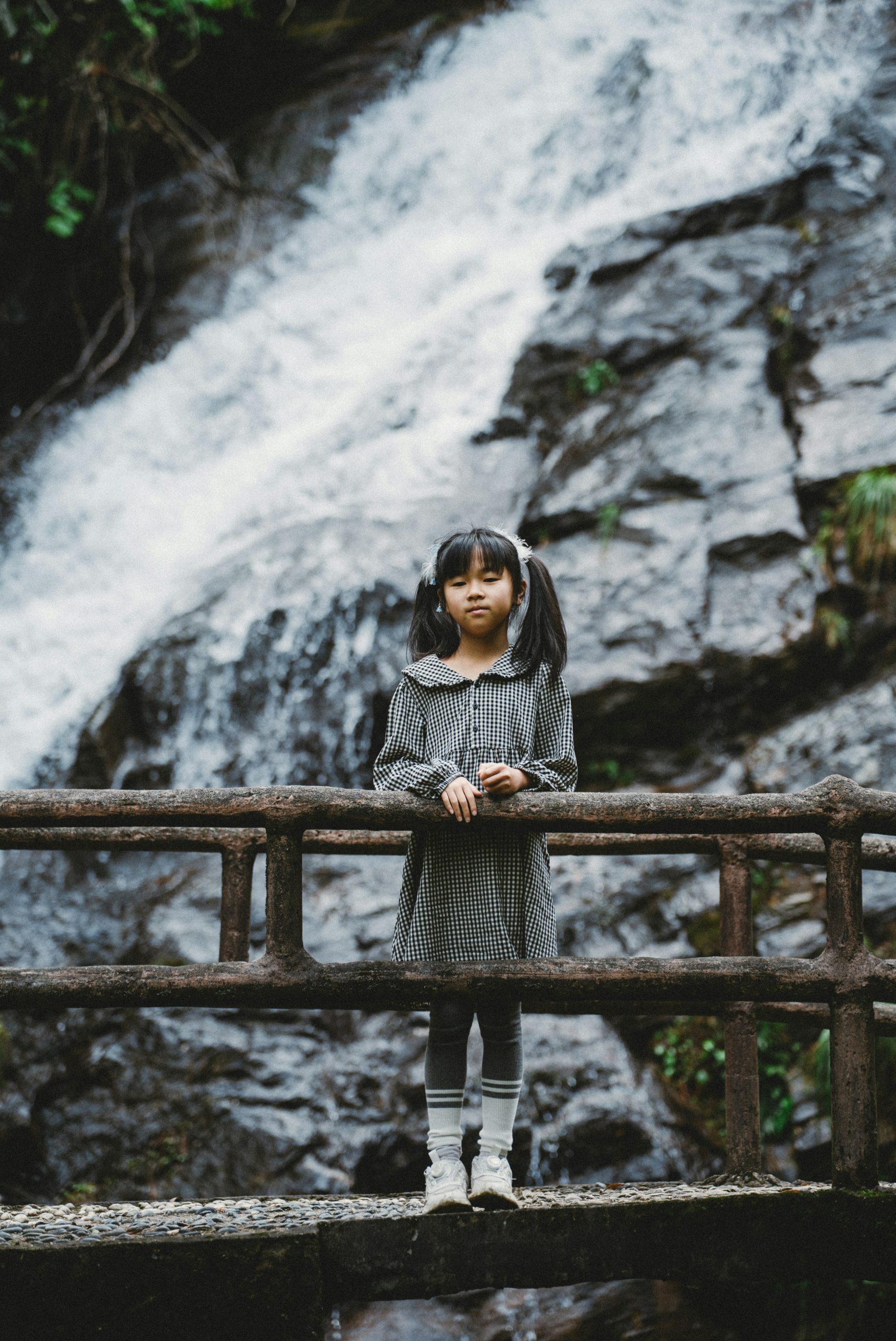 Pigtail girl on a rustic bridge with a cascading waterfall.