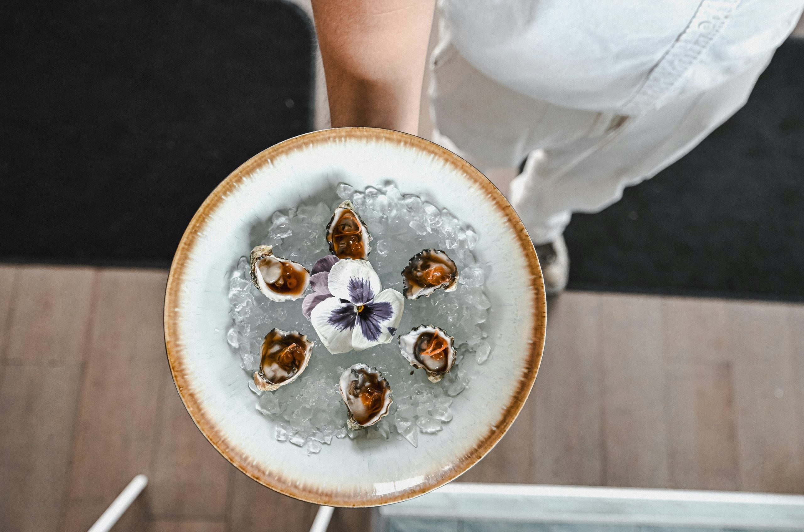 Plate of fresh oysters on ice with a purple flower.