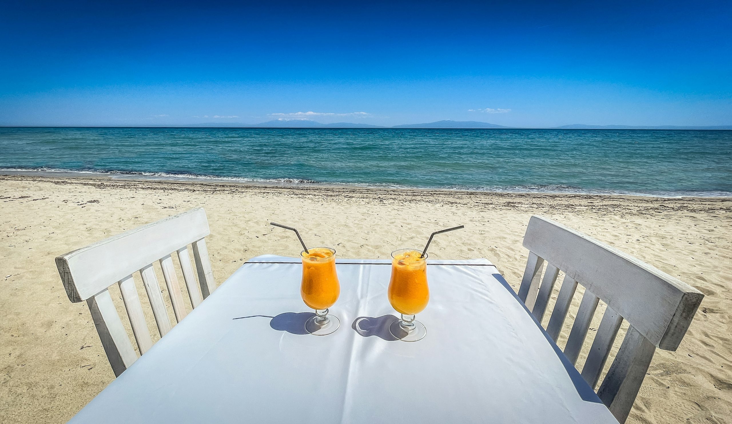 Two orange drinks on a table at a sunny beach.