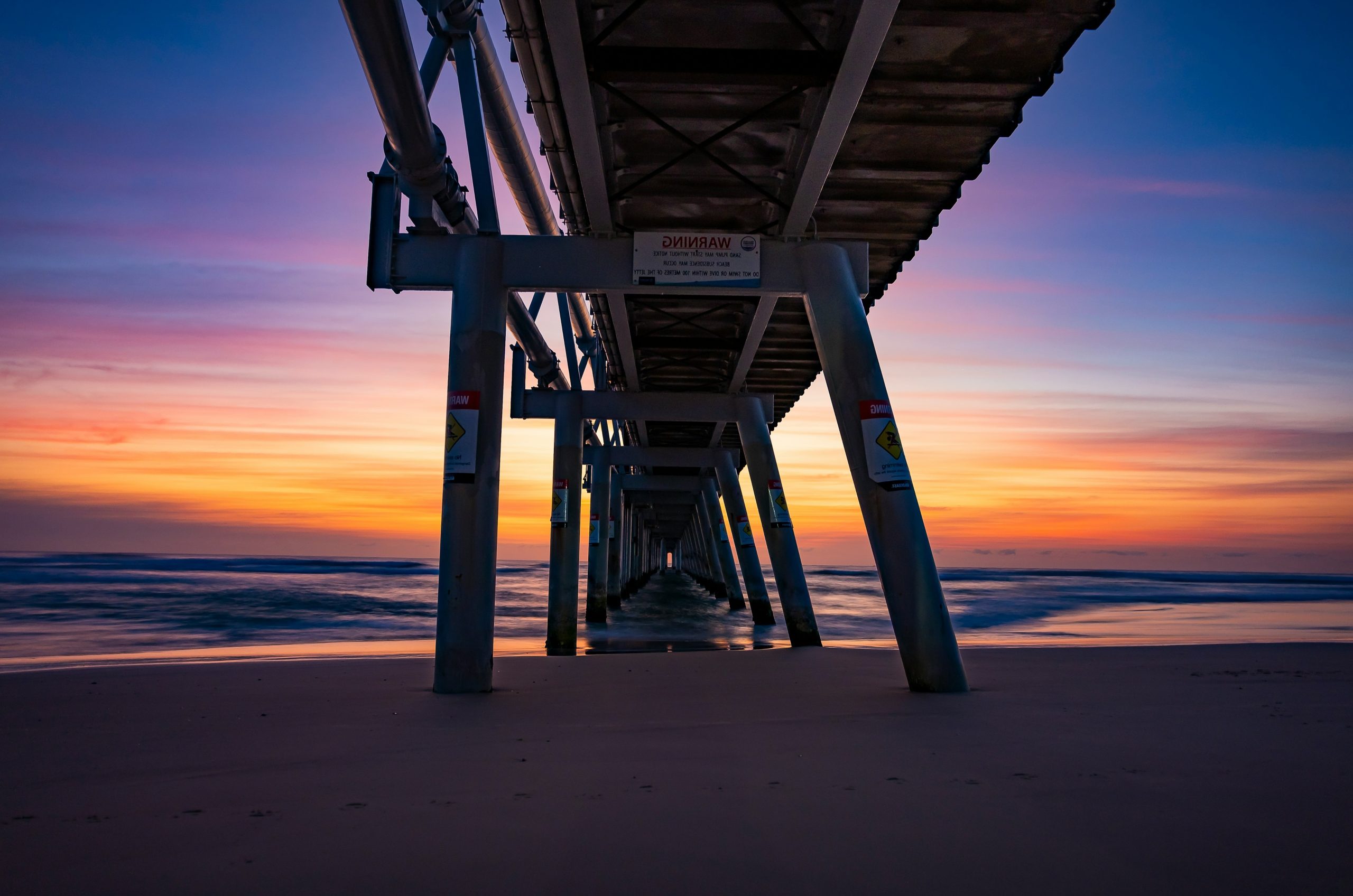 Under a pier at sunset with colorful sky.