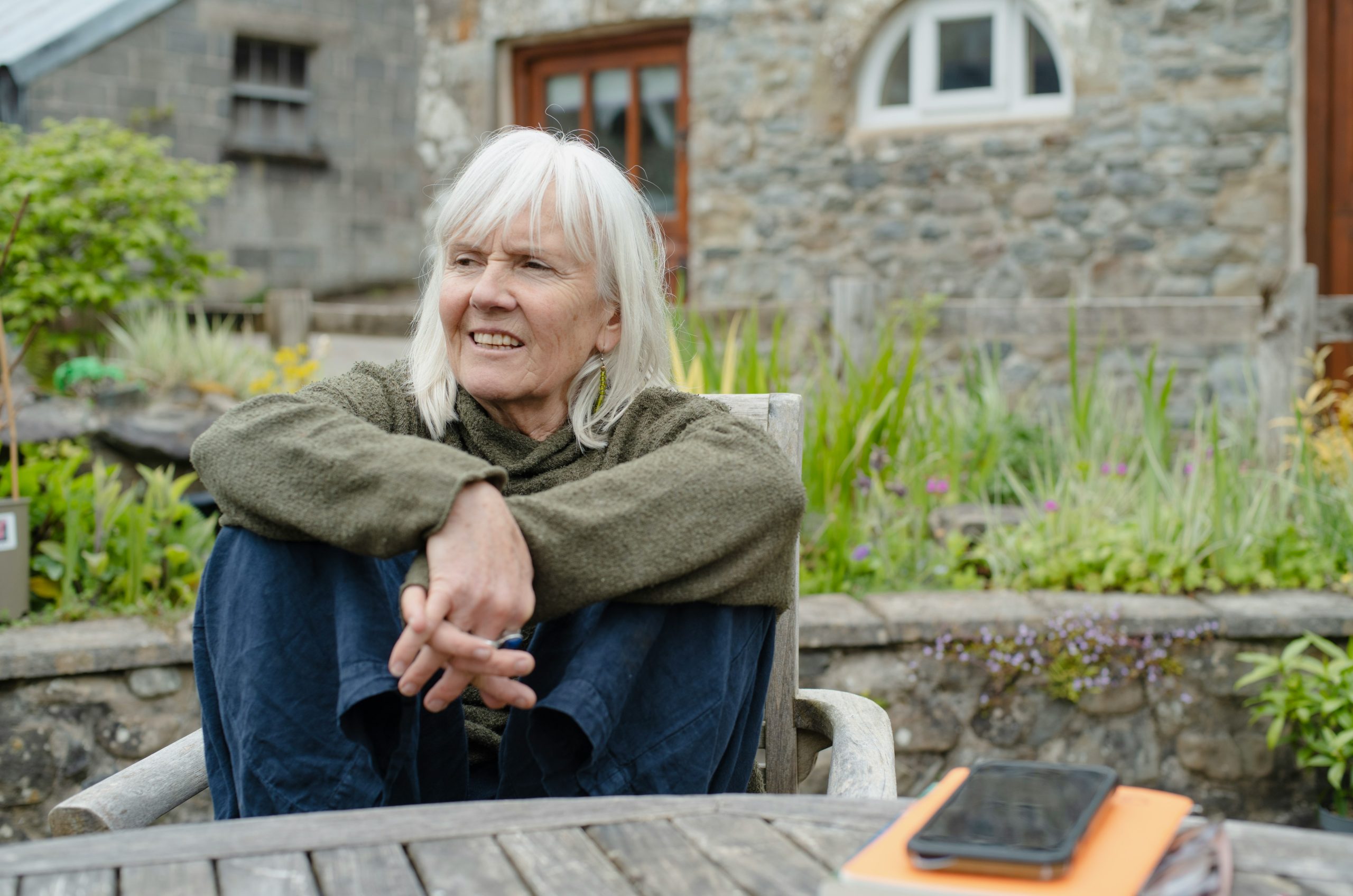 White-haired woman relaxing outdoors with a stone house background.