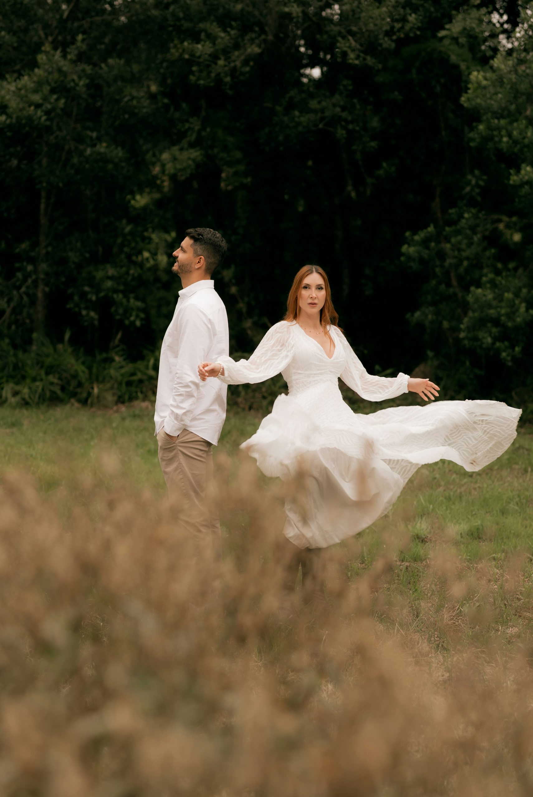 Woman in white dress twirling with man in a field.