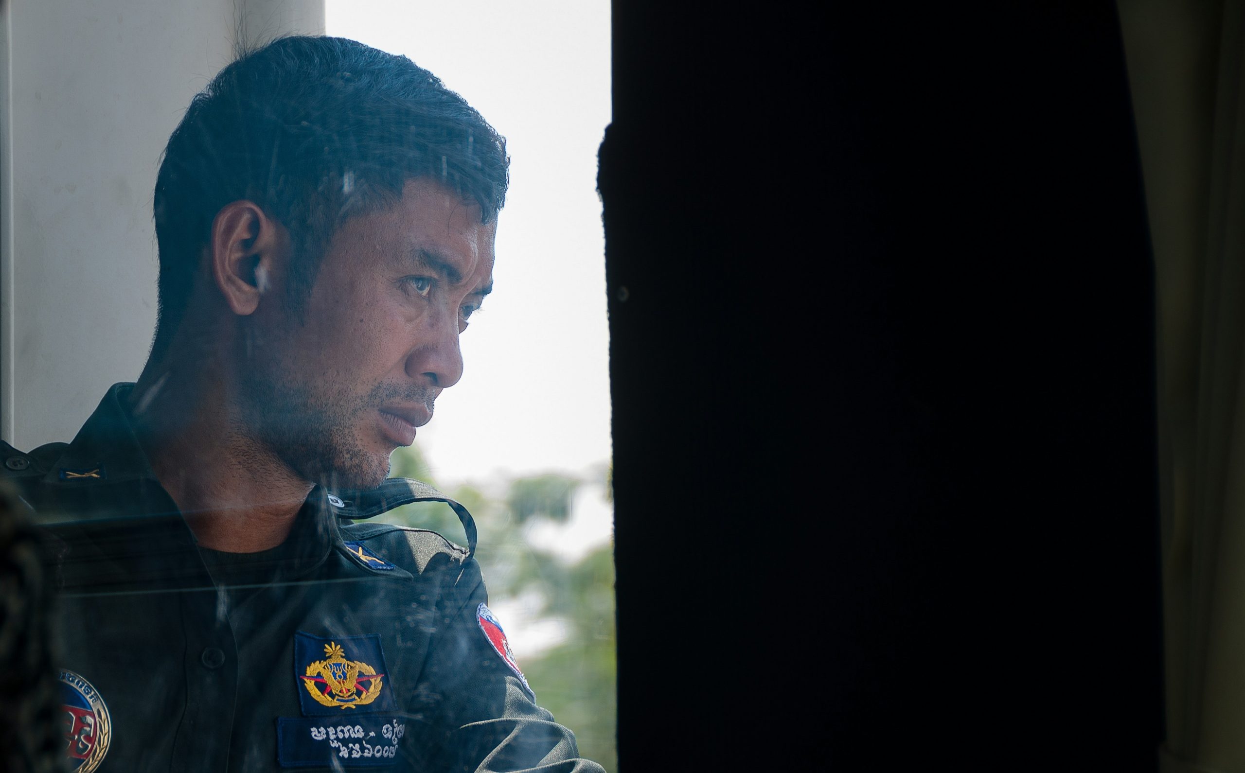 A man in uniform looks thoughtfully out a window.