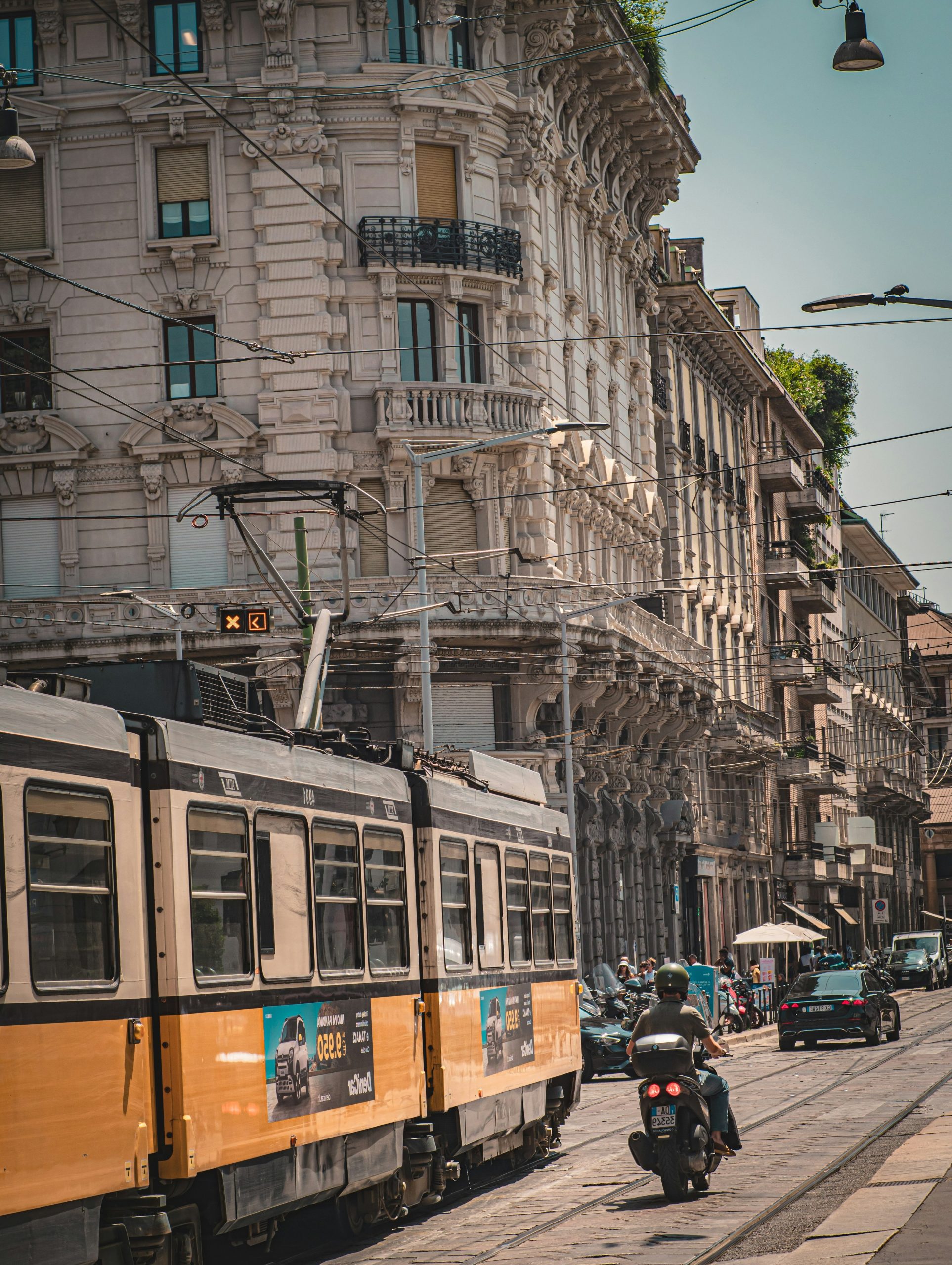 A yellow tram and scooter on a sunny city street.