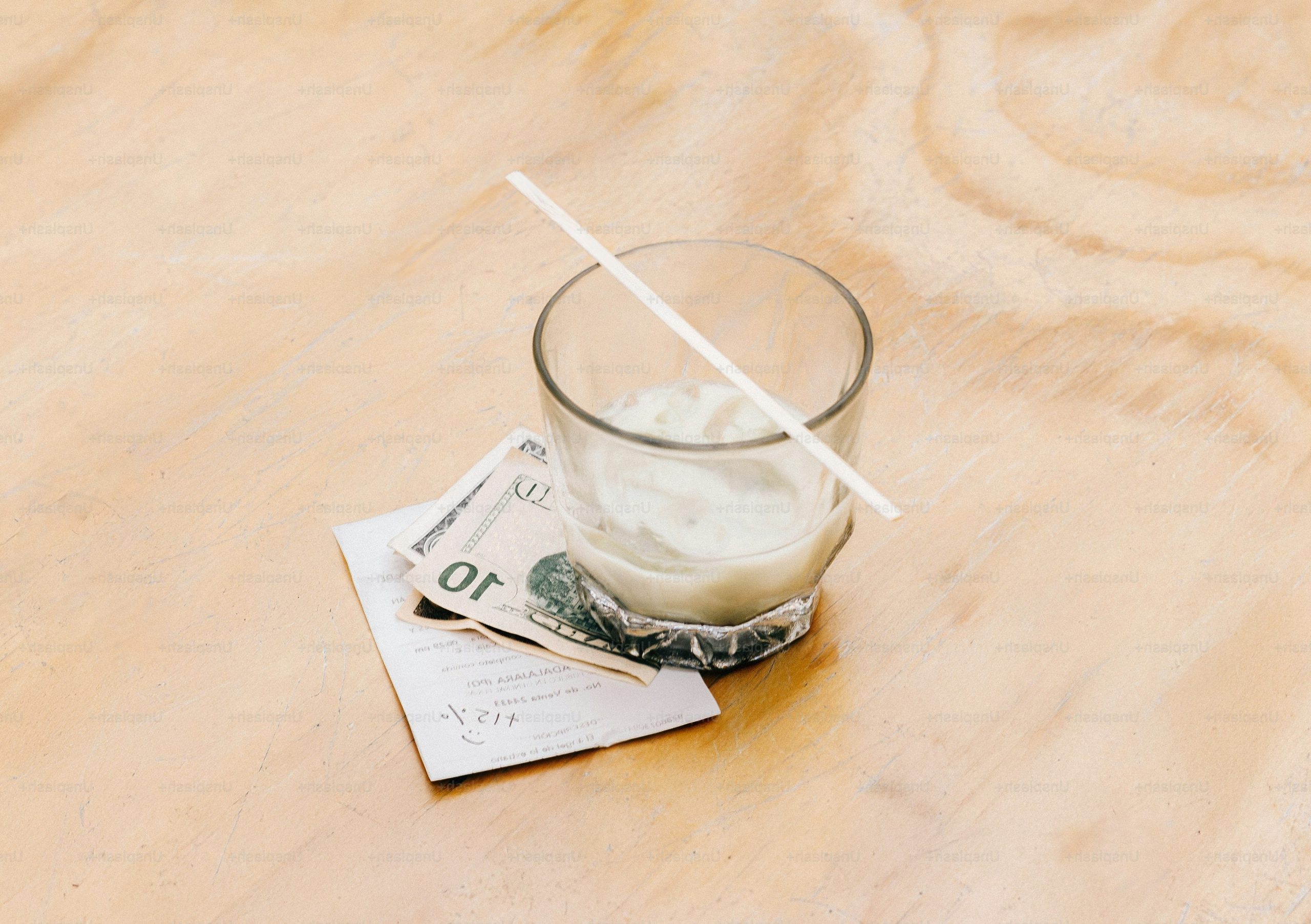 Glass with straw and dollar bill on light wood.