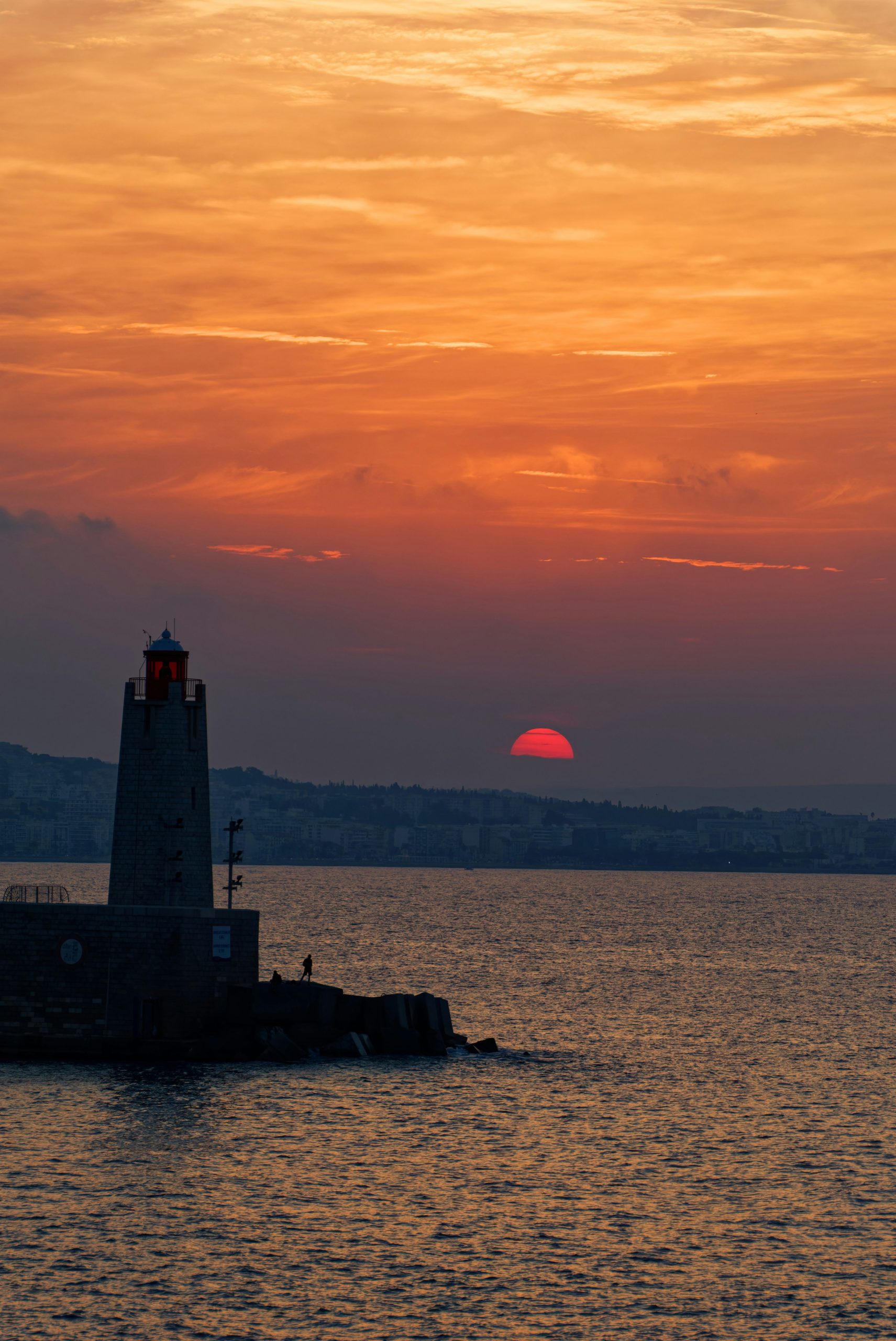 Lighthouse silhouette against a fiery red and orange sunset sky.