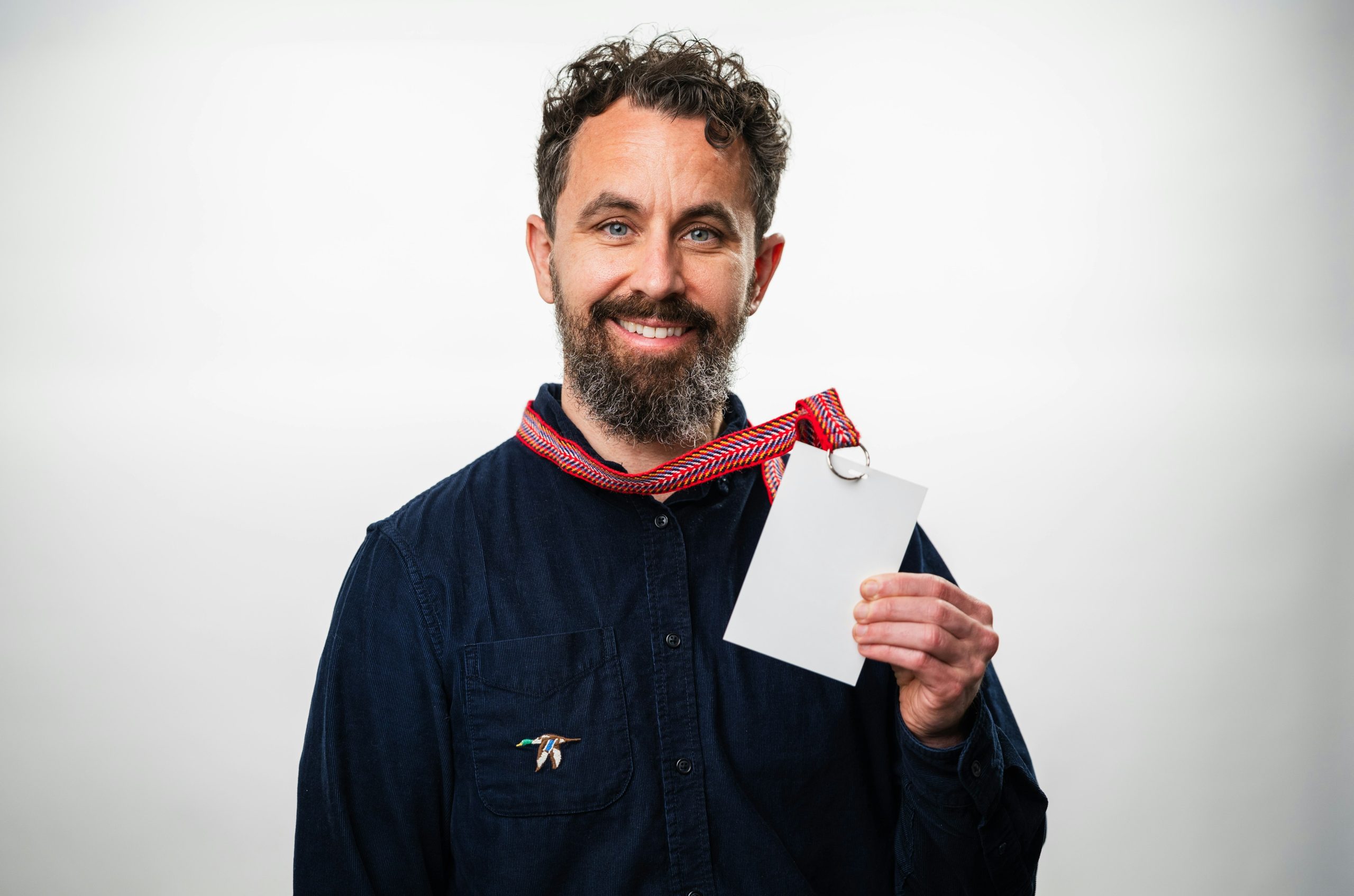 A man with a beard wearing a dark shirt holding a blank white badge.
