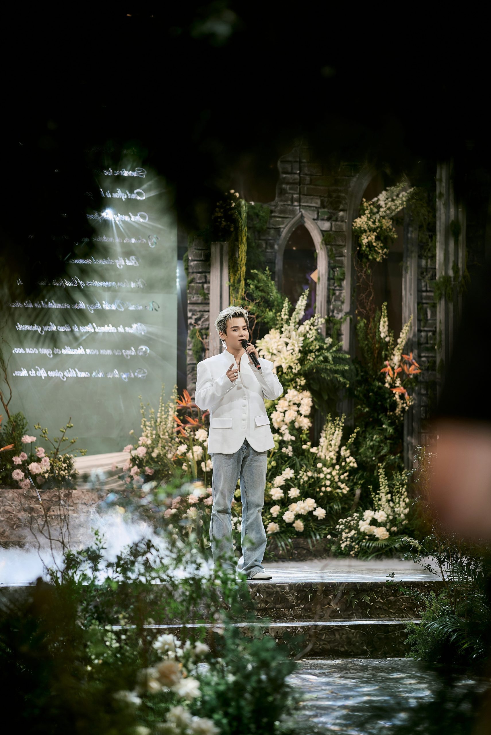 Man performs on an elaborate stage adorned with white flowers.