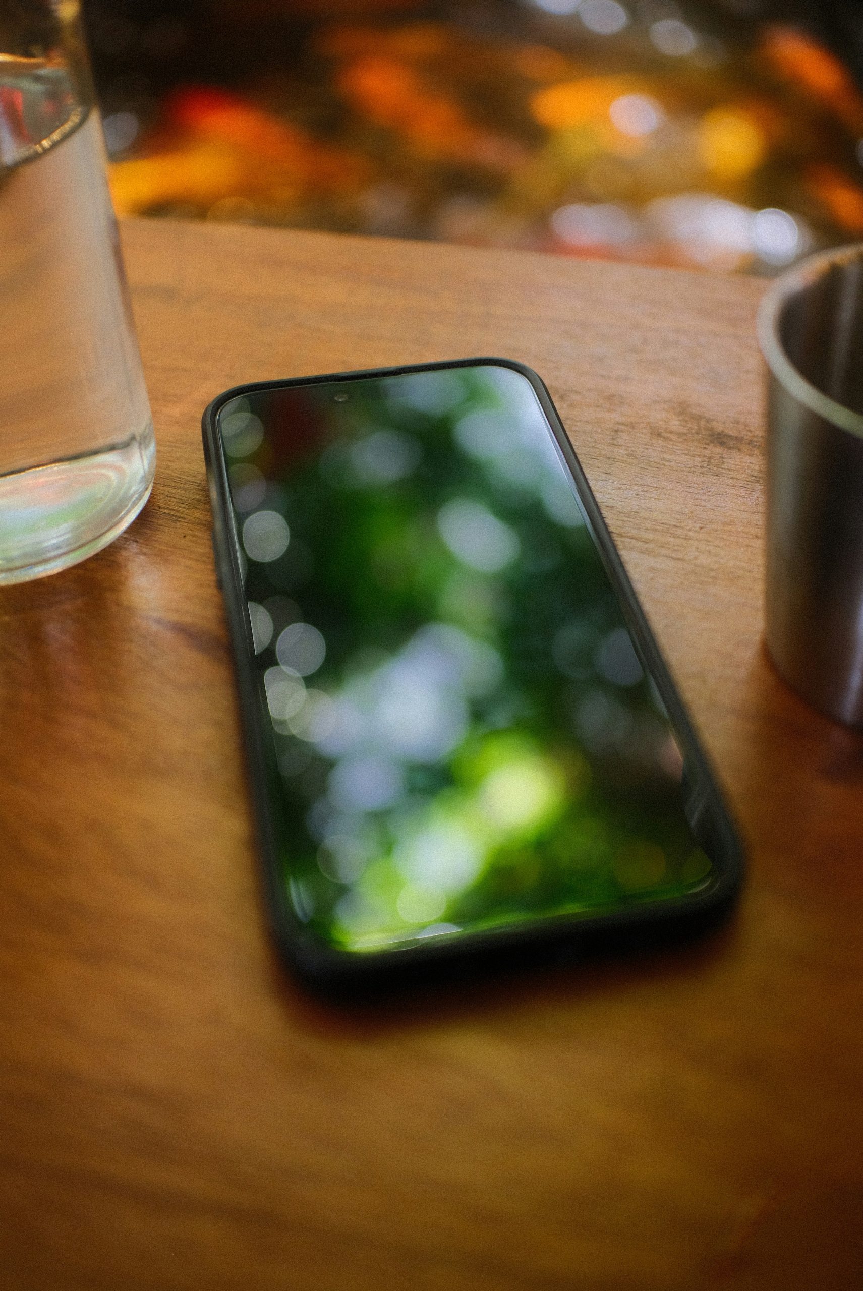 Mobile phone on wooden table reflecting green bokeh.