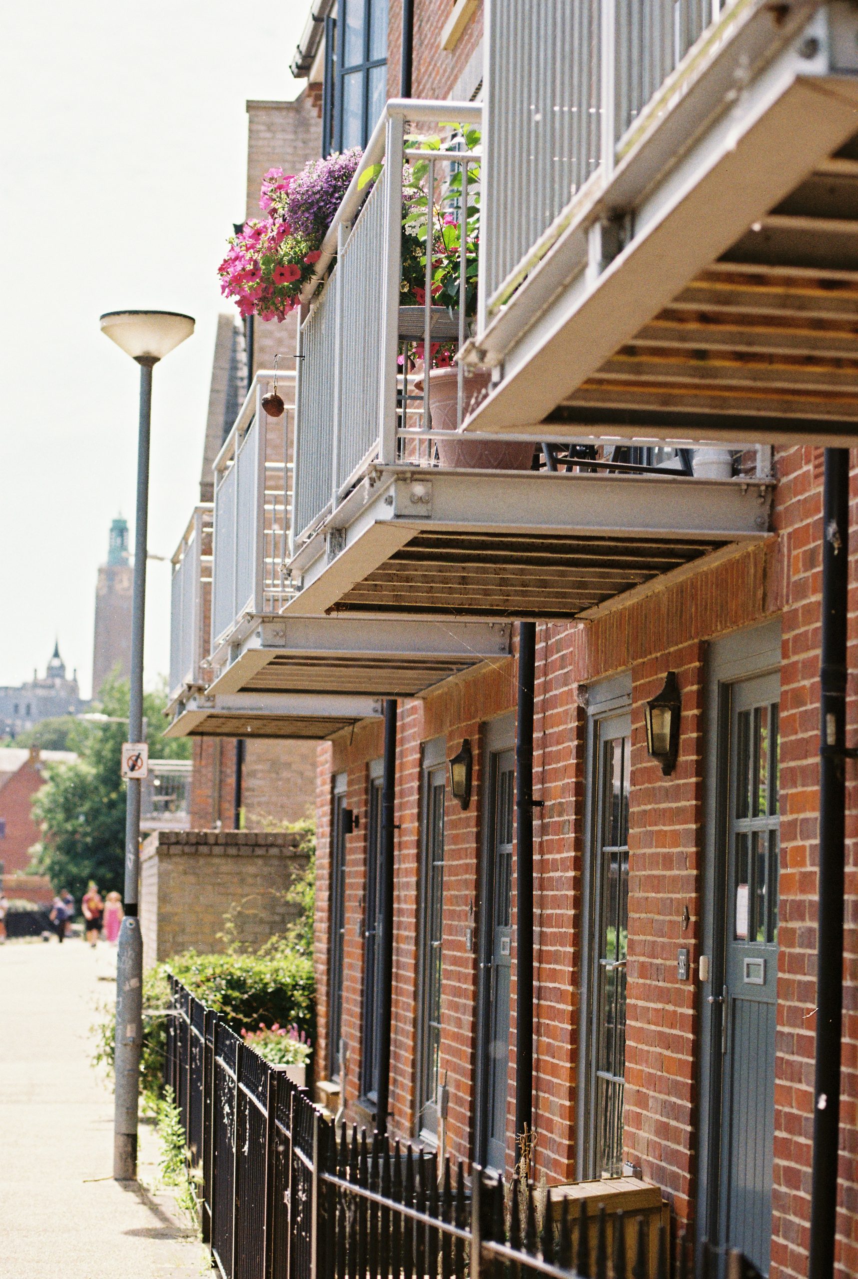 Modern brick buildings featuring metal balconies with potted flowers.
