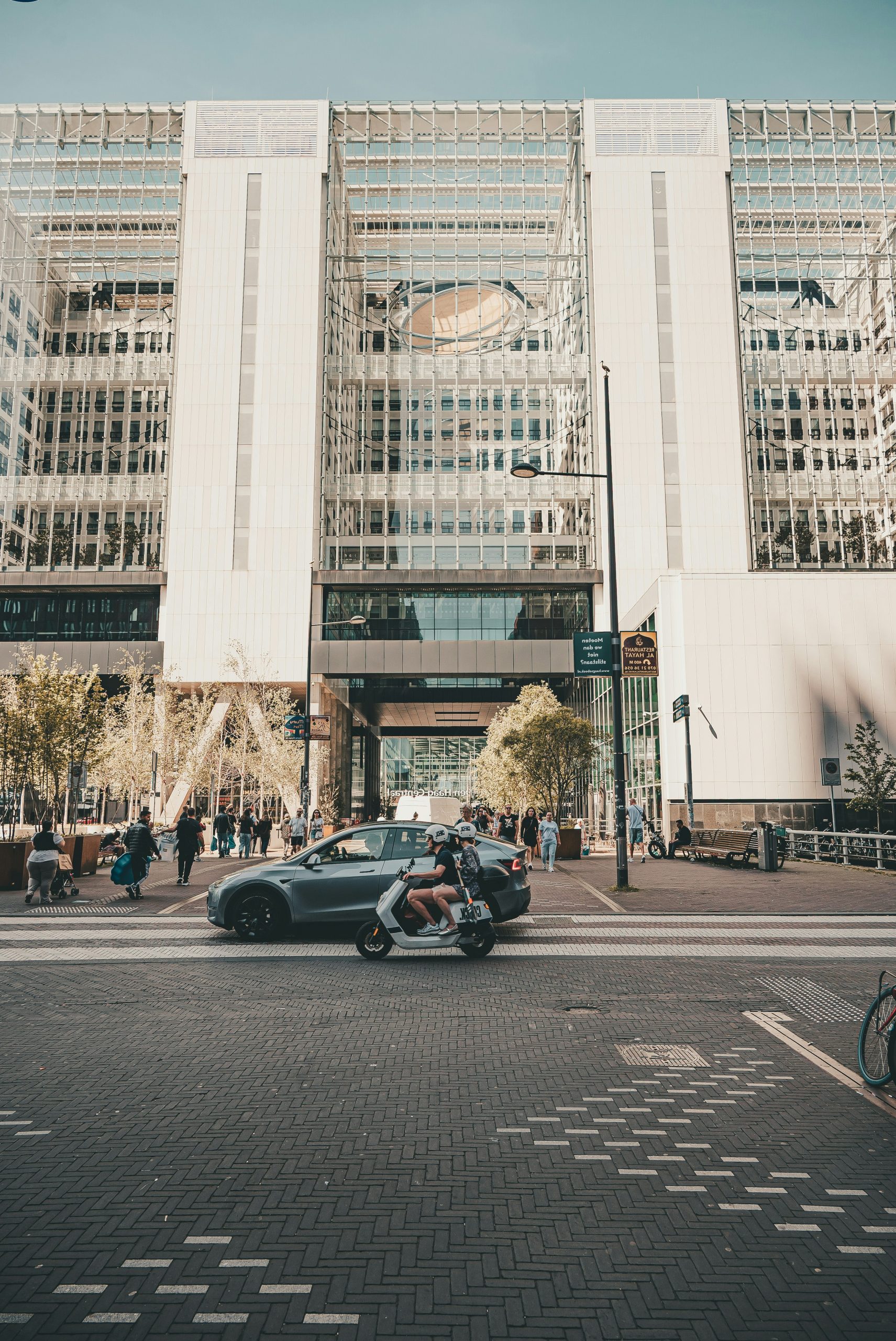 Modern building, car, and scooter on a busy city street.