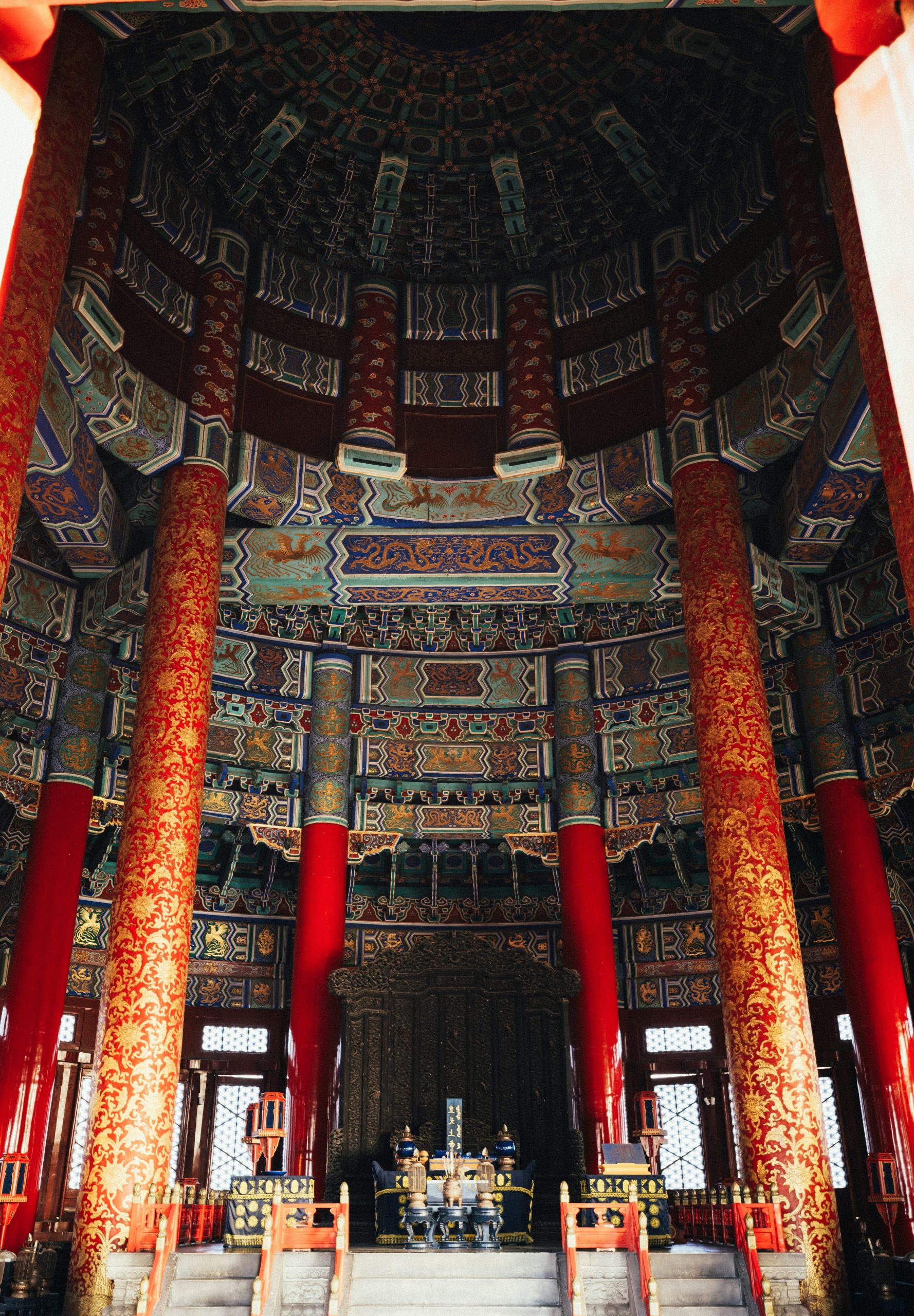 Ornate temple interior with red pillars and decorated ceiling.