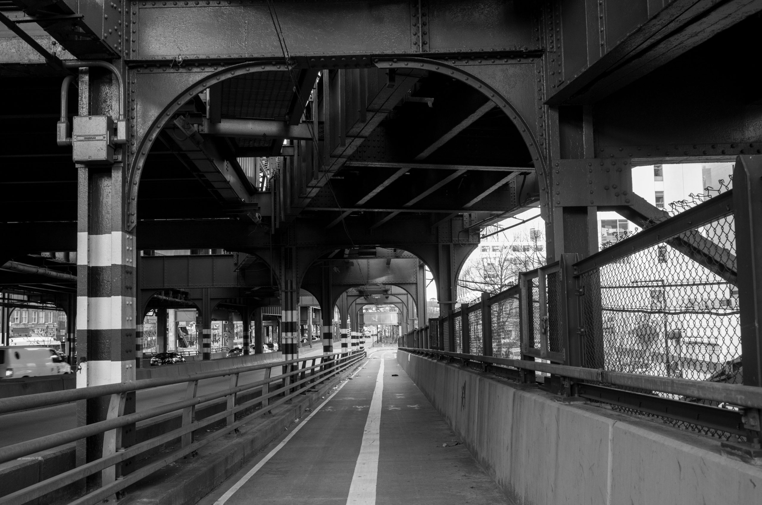 Pathway beneath a large, elevated urban bridge in monochrome.