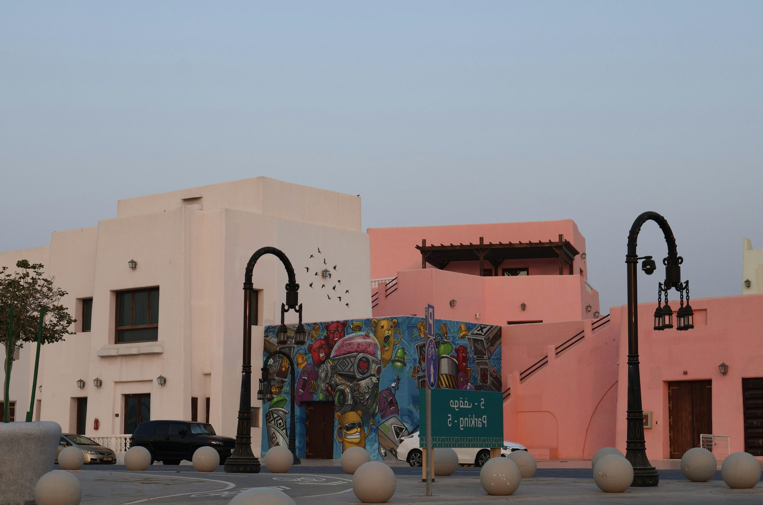 Pink and beige buildings with streetlights and a colorful mural.