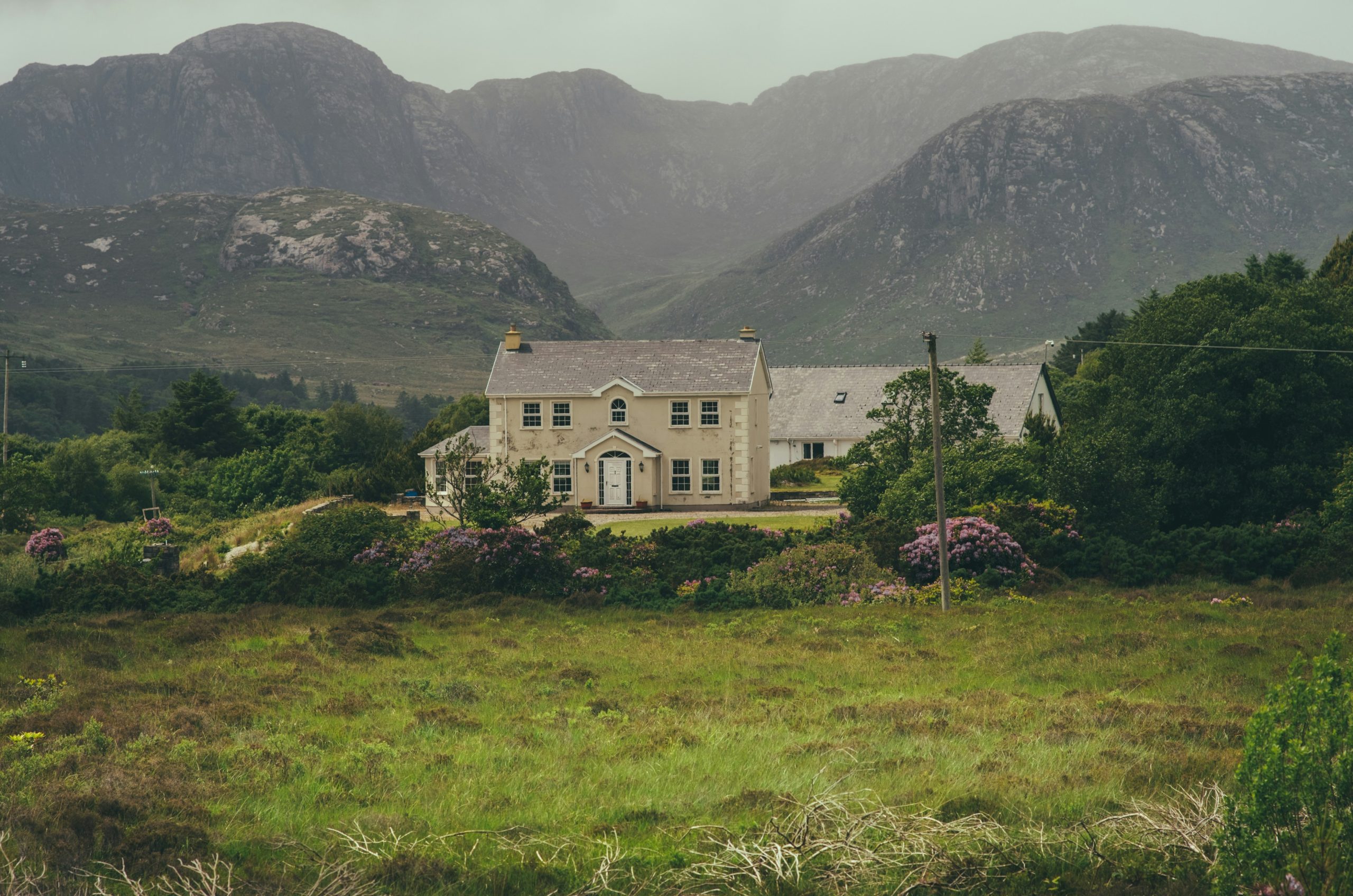 Rural stone house amidst green fields and misty mountains.