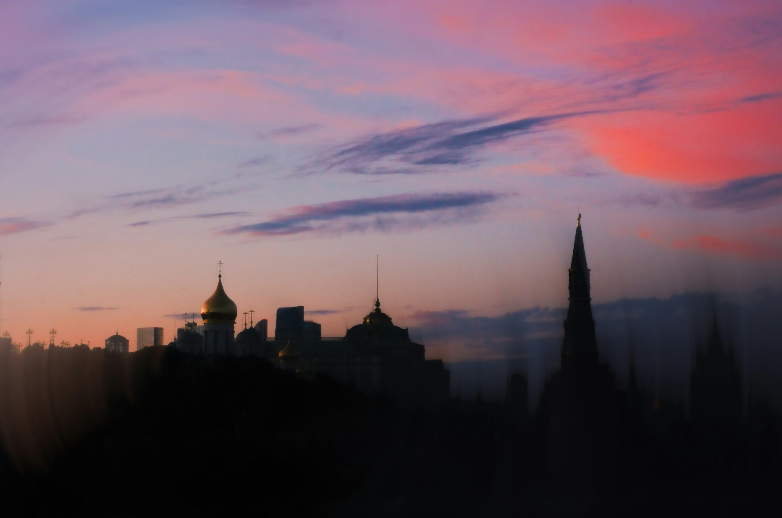 Silhouetted city skyline under a colorful pink and purple sunset.