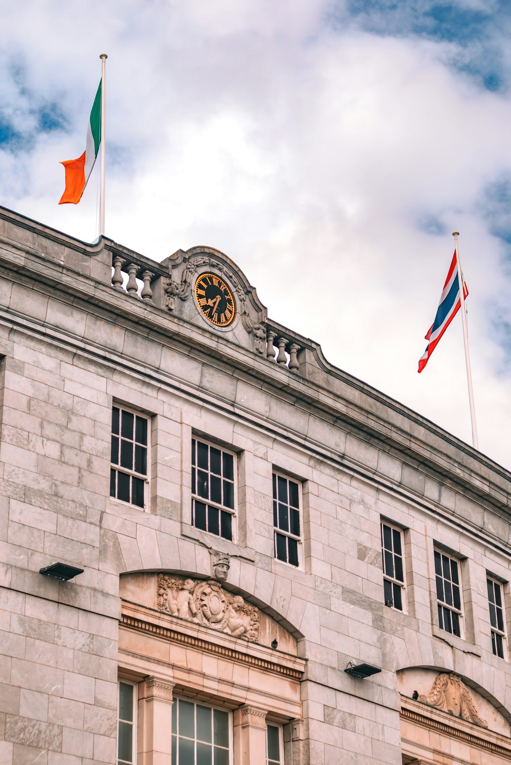 Stone building with thai and irish flags under cloudy sky.