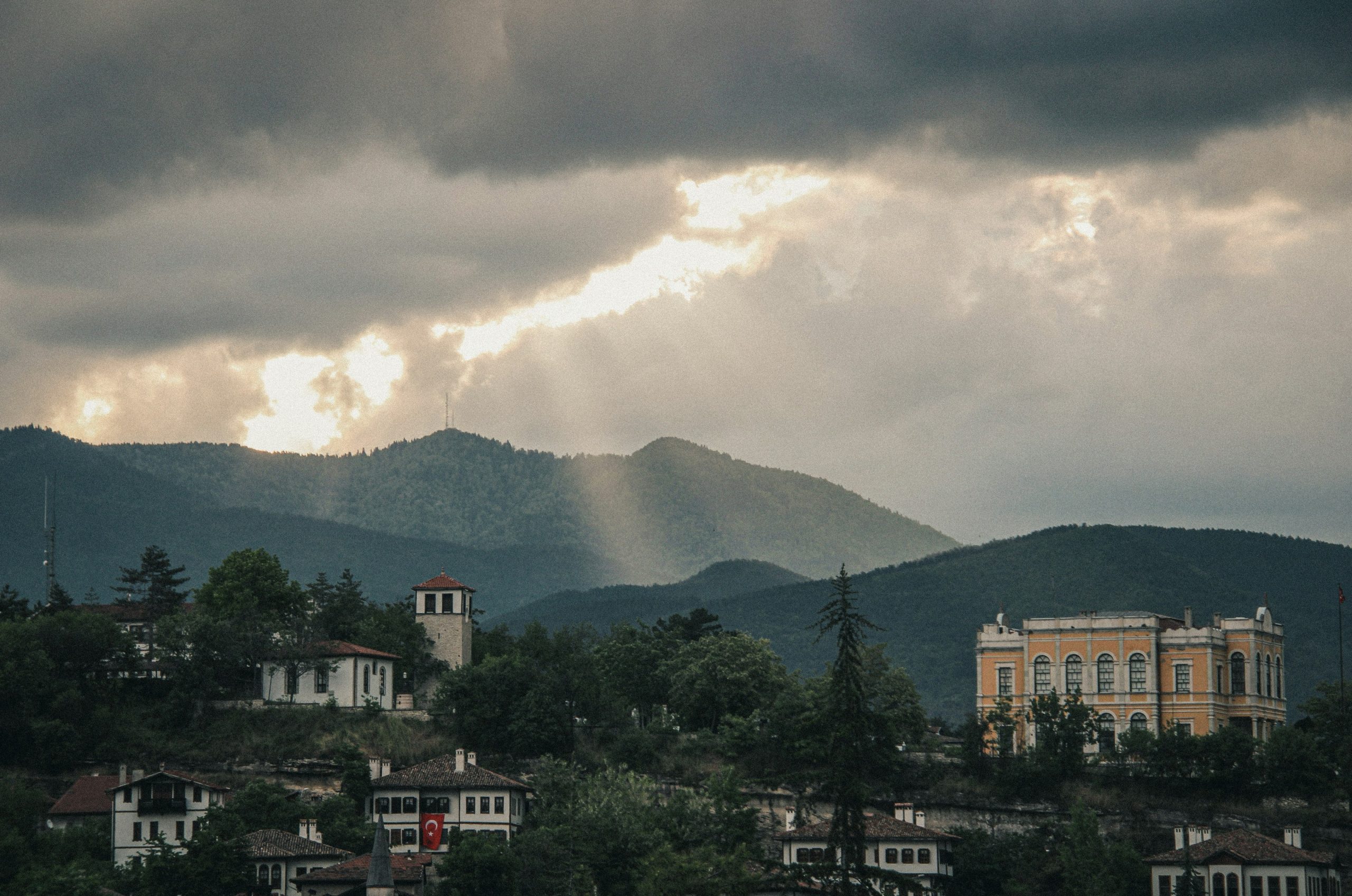 Sun rays pierce dramatic clouds over a town and mountains.