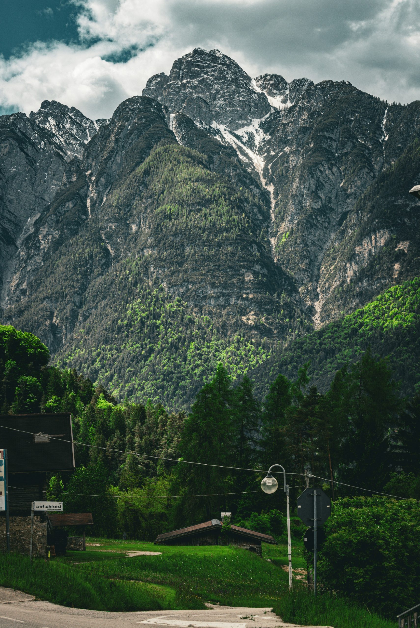 Towering mountains with snow and trees overlooking a small road.