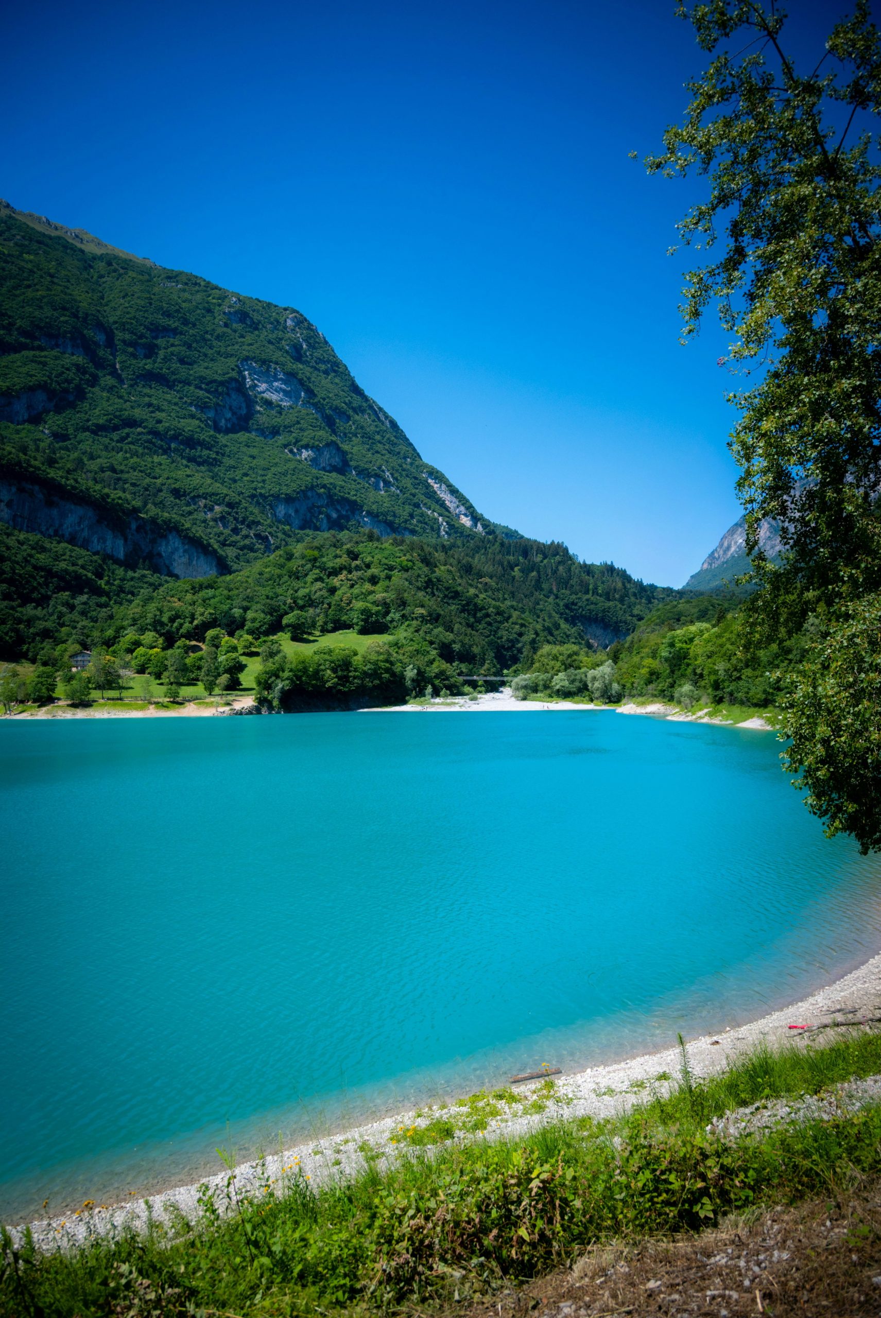 Turquoise lake beside lush green mountains and clear blue sky.