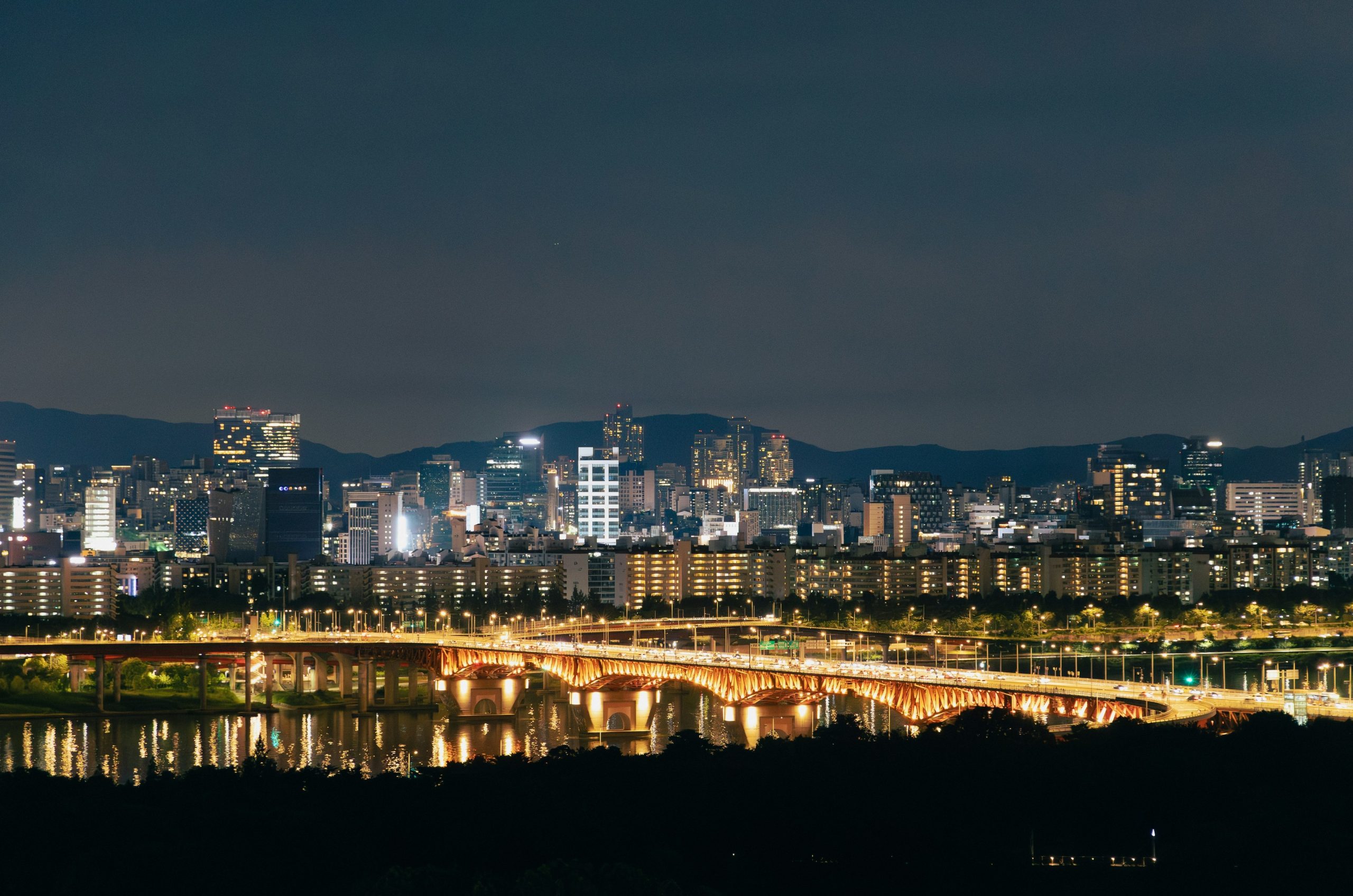 Vibrant cityscape at night with a lit bridge over water.