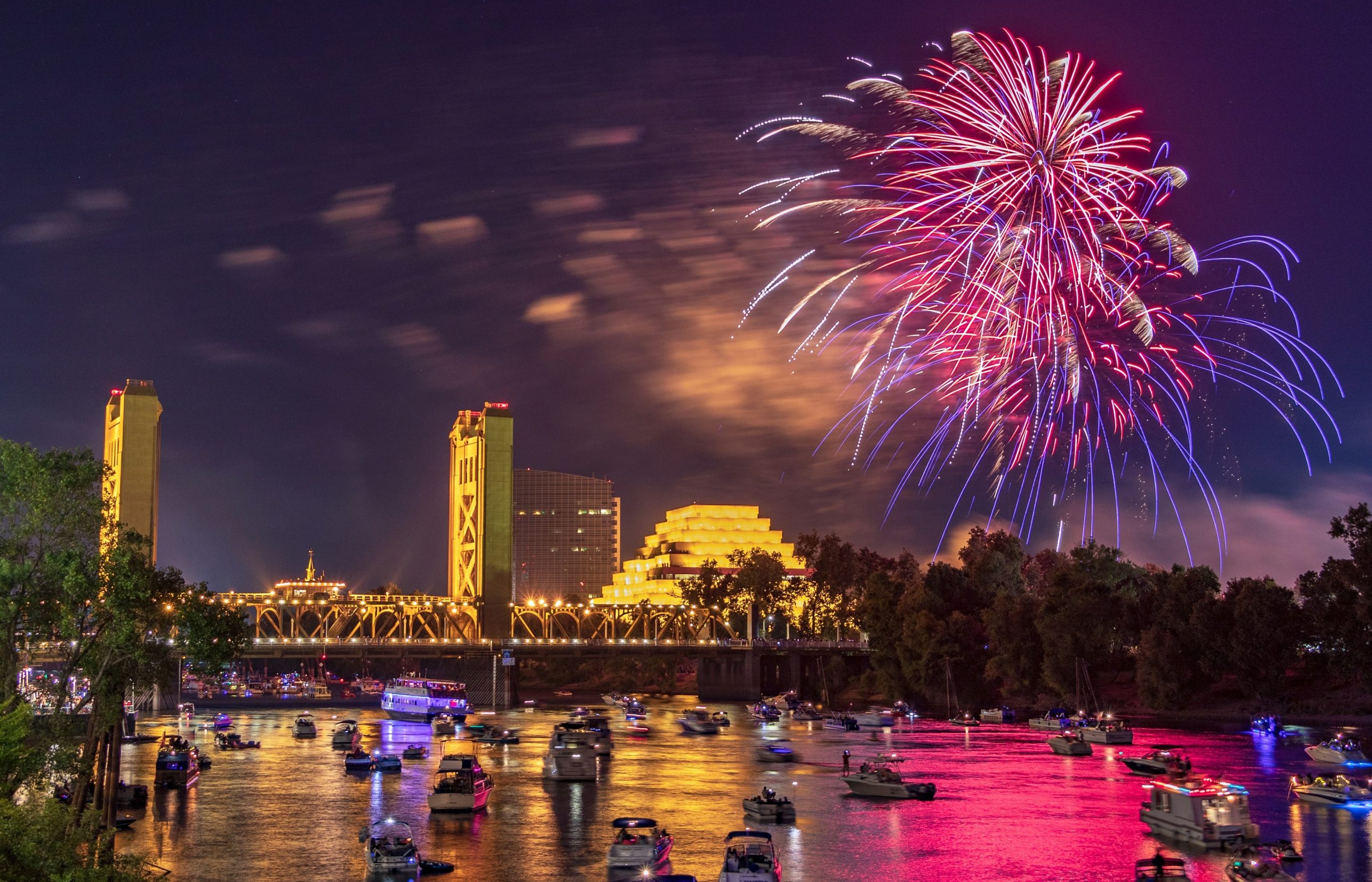 Vibrant fireworks illuminate a city skyline and river with boats.